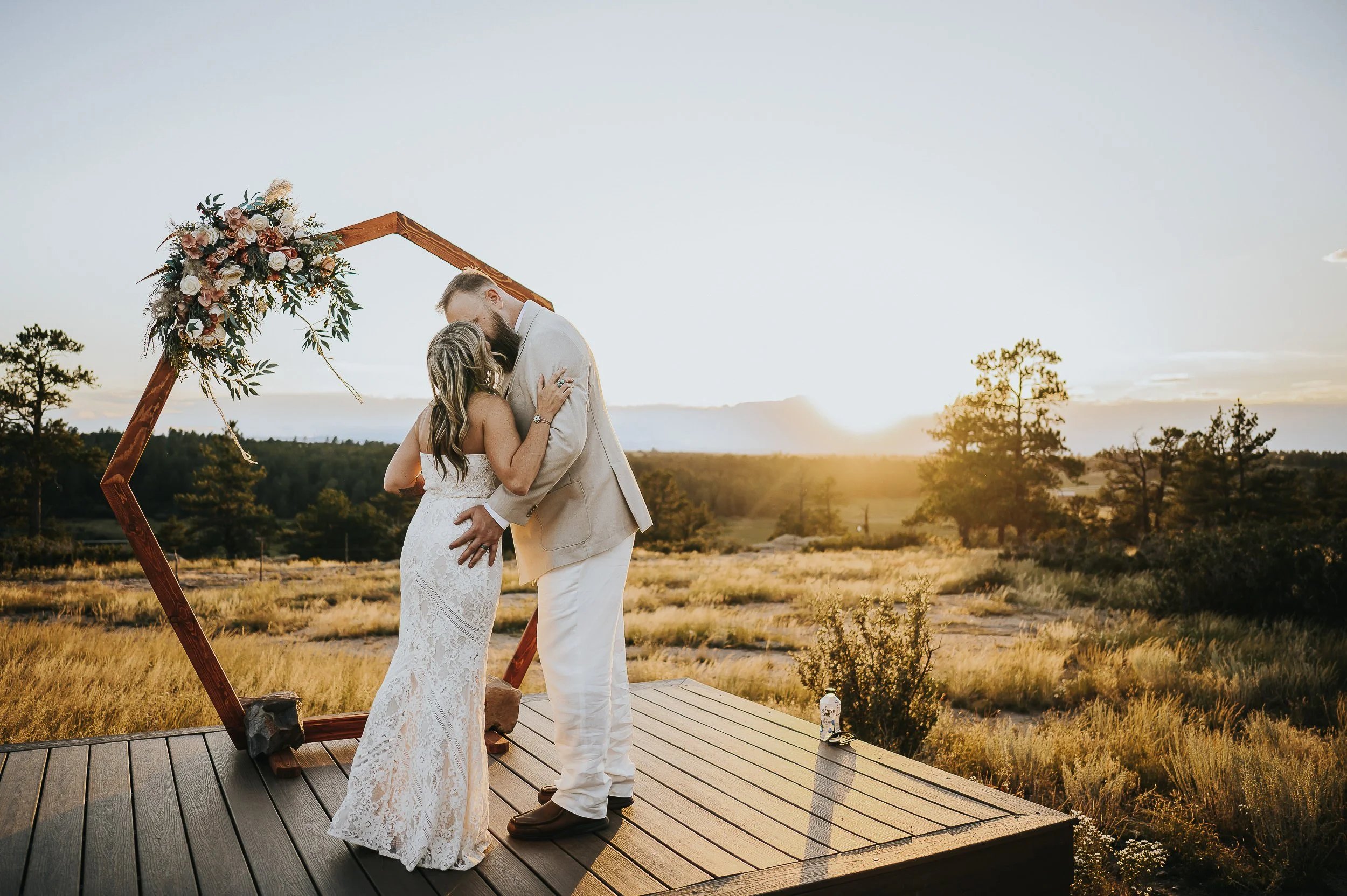 A couple exchanges vows on a wooden platform at golden hour, mountains glowing behind them at Castlewood Canyon State Park.