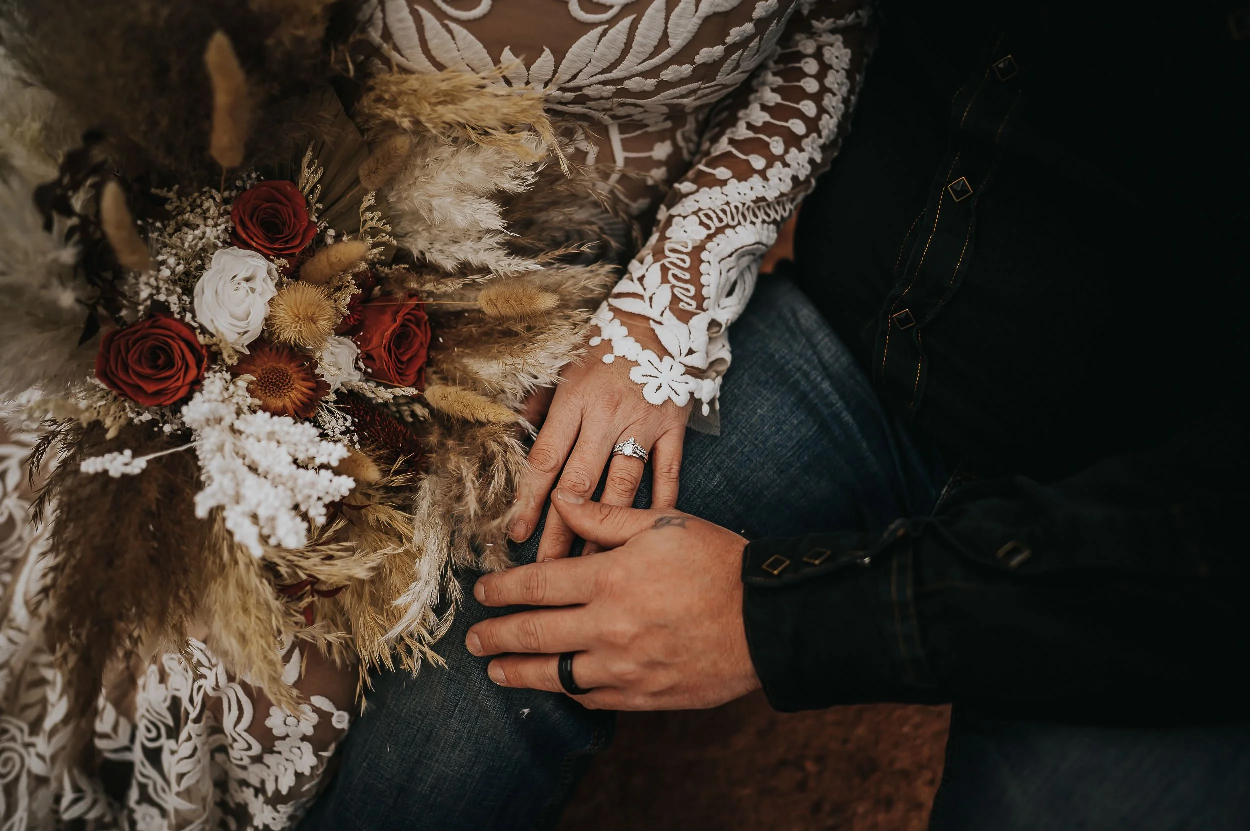 A couple embraces closely, her lace sleeve and his tattooed arm visible, intimate and tender.