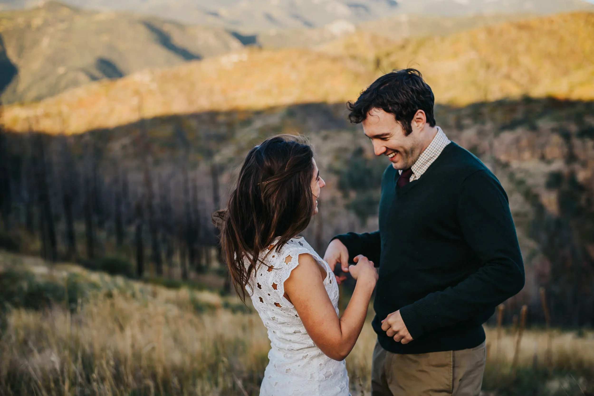 A couple shares a quiet moment together in the Colorado mountains, she in a white dress, he in a sweater on Rampart Range Road.