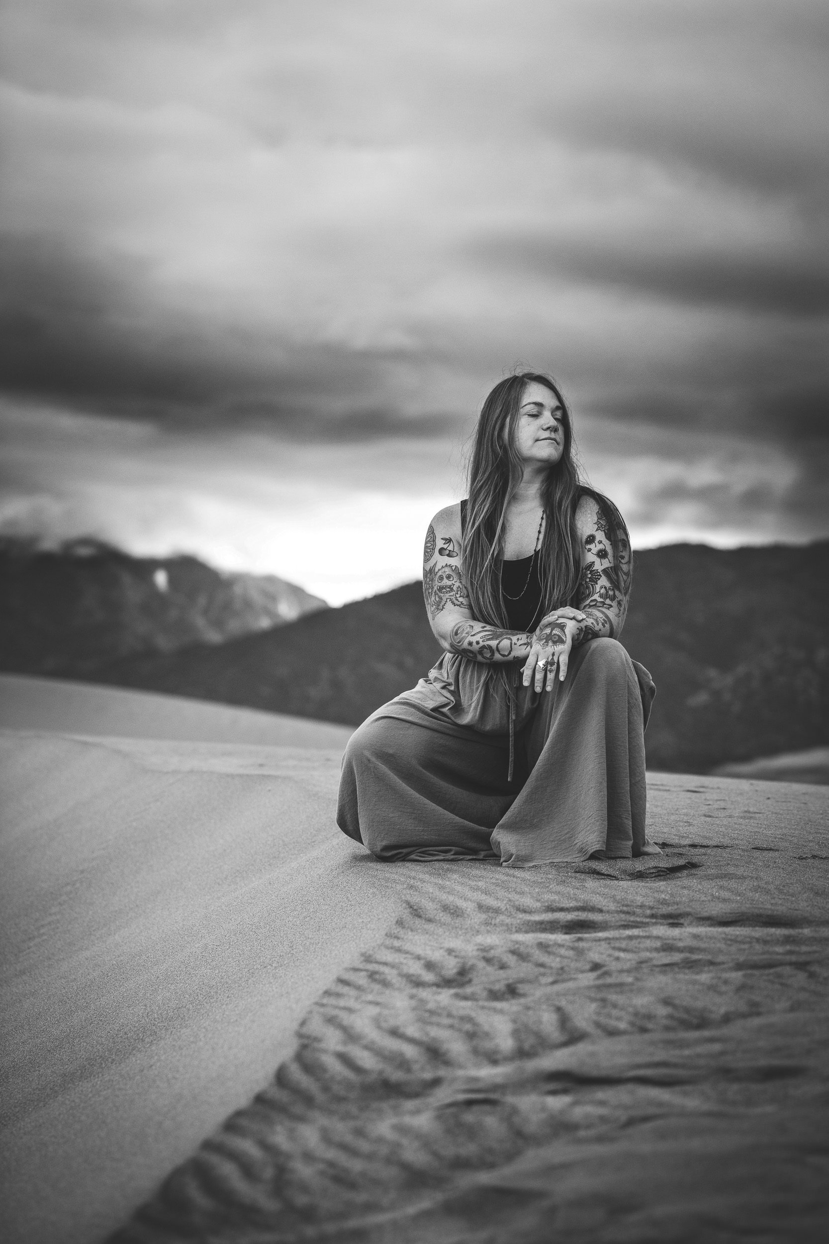 Sandy, a Colorado Elopement photographer closes her eyes while she kneels down in the sand at The Great Sand Dunes National Park.