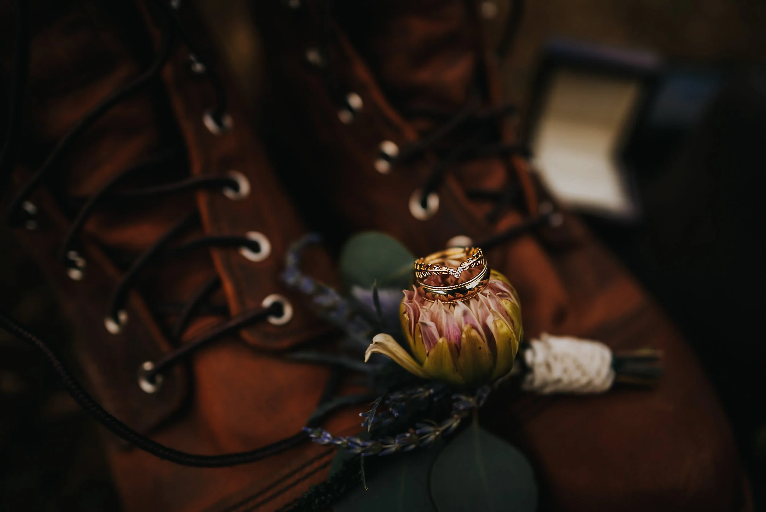 A wedding detail closeup of a ring resting against leather boot laces and a dried floral.