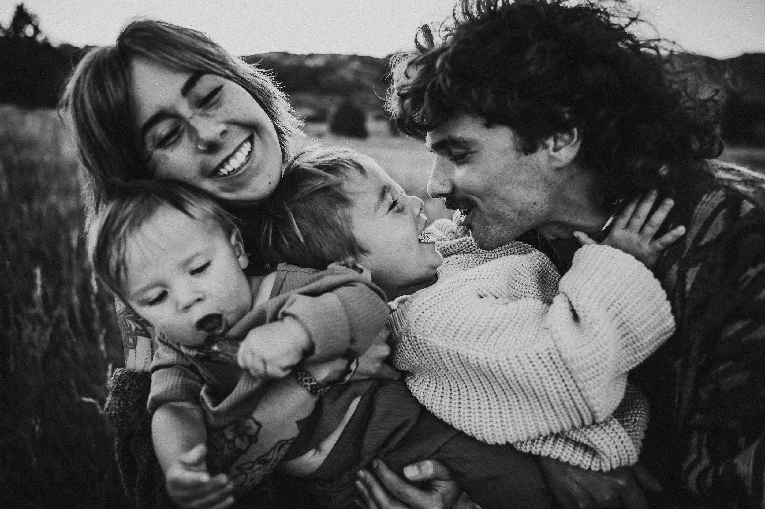A mother smiles widely as her family holds her during their family photo session.