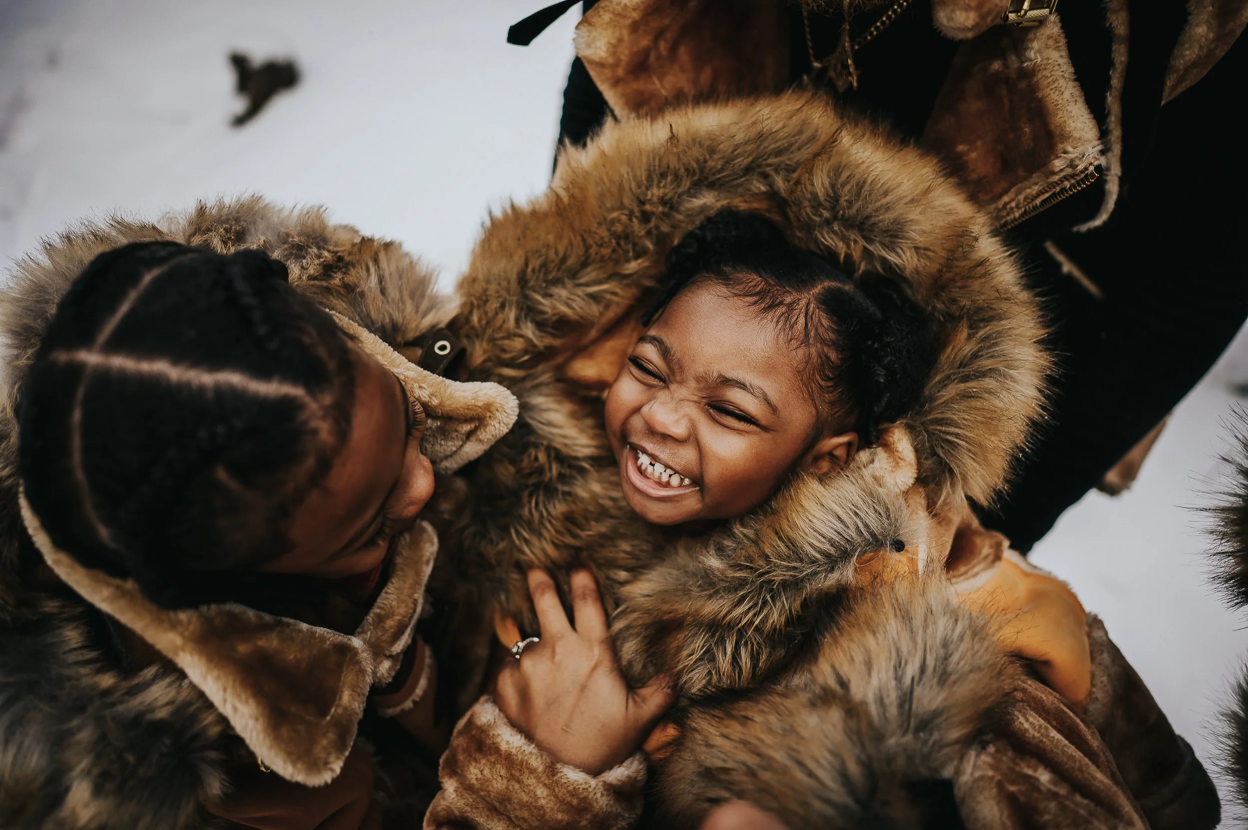 Mom and daughter laughing together in caramel faux fur coats during a winter family session in Colorado.
