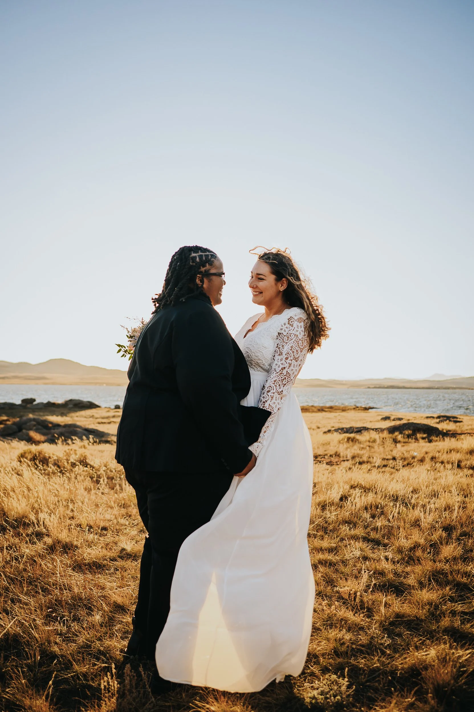 Two brides standing together in the mountains near Lake George before their ceremony.
