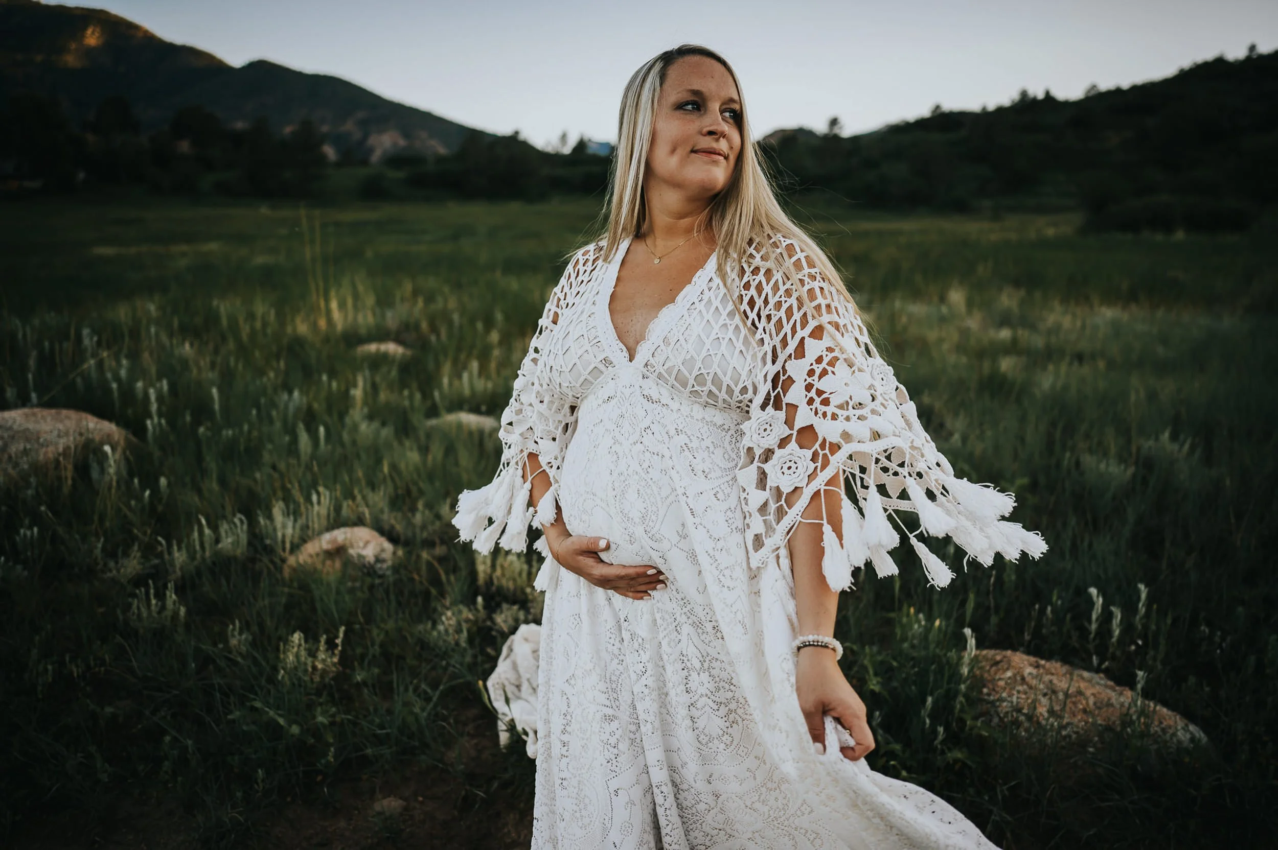Woman in white crochet macrame shawl standing in a green Colorado meadow at dusk, showcasing texture in family photo outfits.