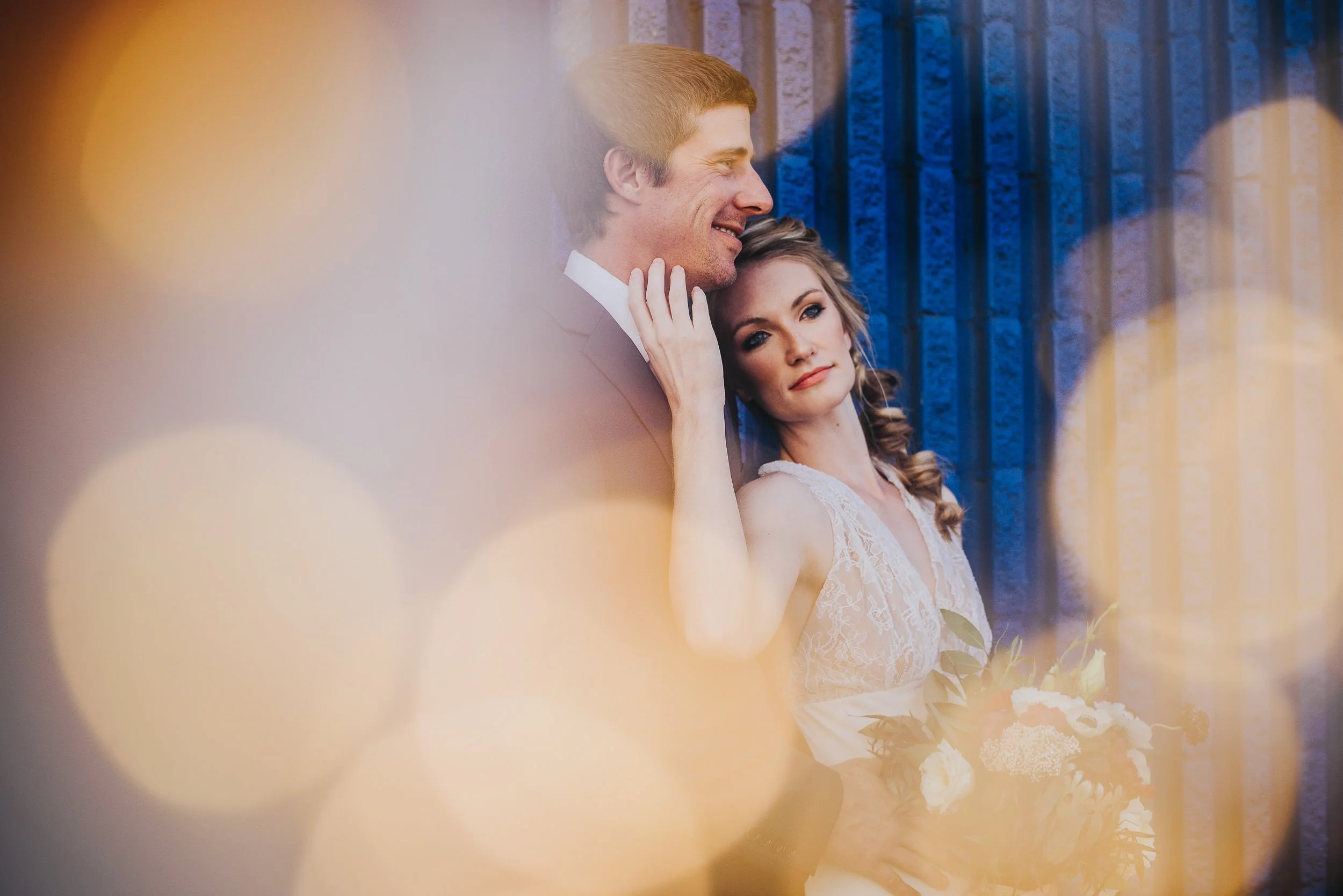 A couple laughs together in golden light near a blue barn door, she in a lace gown.