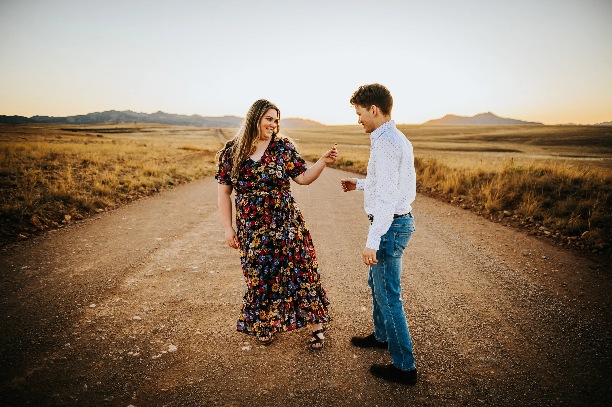 A couple dances together on a dirt road through wide open Colorado ranchland, she in a floral dress.