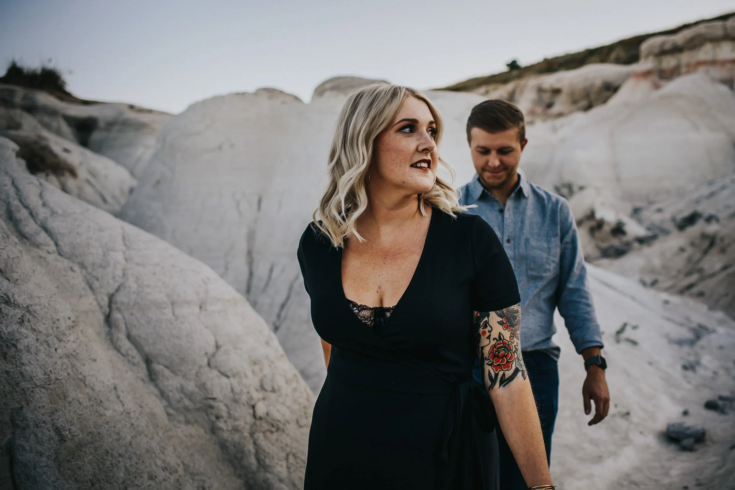 A couple walks together through a white rock landscape, she holds a drink, relaxed and easy.