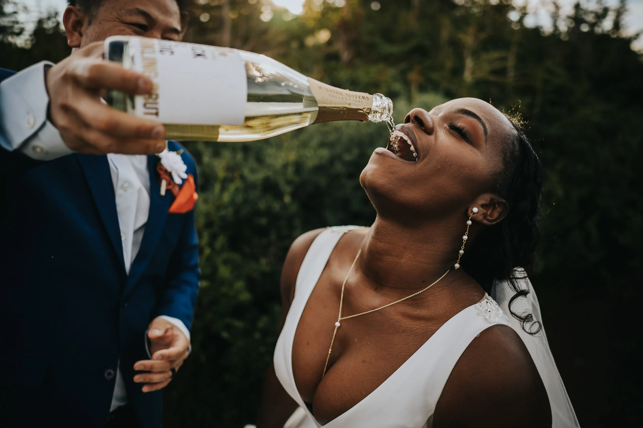 A bride throws her head back laughing as champagne spills, pure celebration energy.