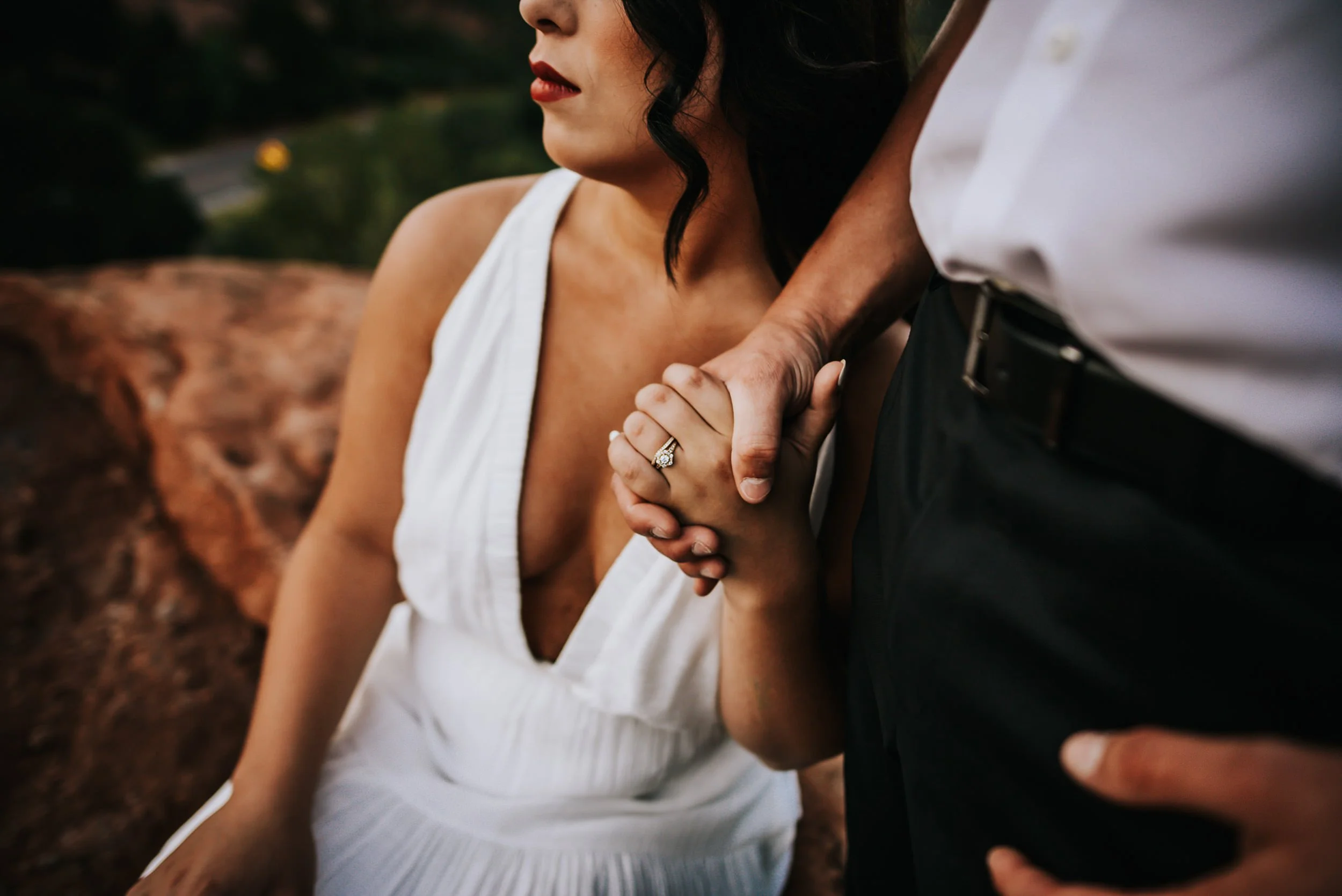 A closeup of a couple's hands clasped together, she in a white halter dress, standing close.