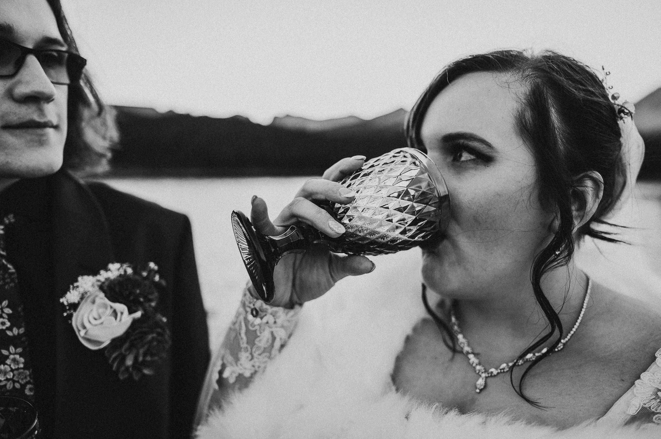 A bride drinks from a chalice, laughing, black and white portrait at Brainard Lake.