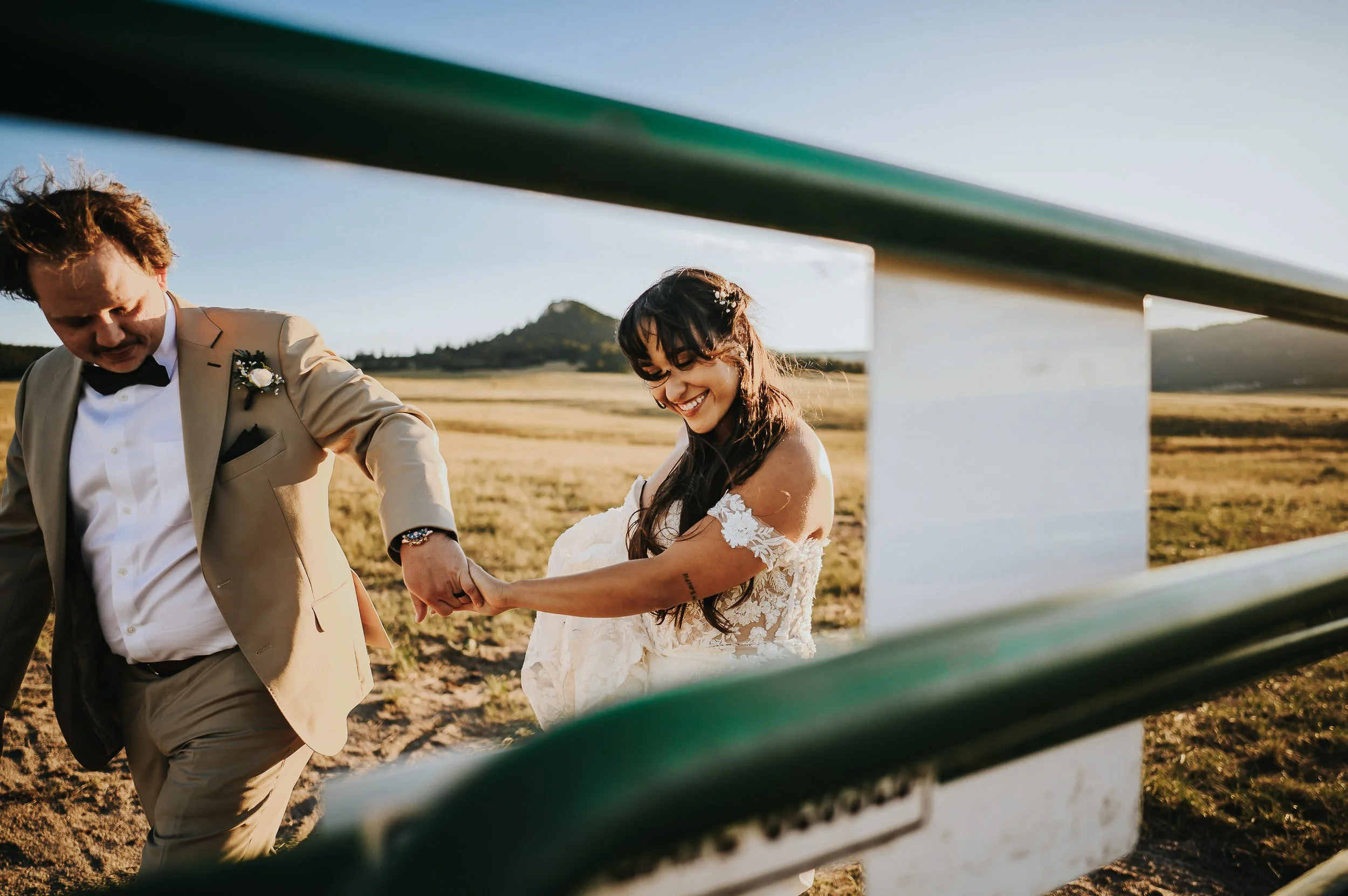 A woman walks through a field, her partner next to her, laughing and playful, shot through a fence for depth of field.