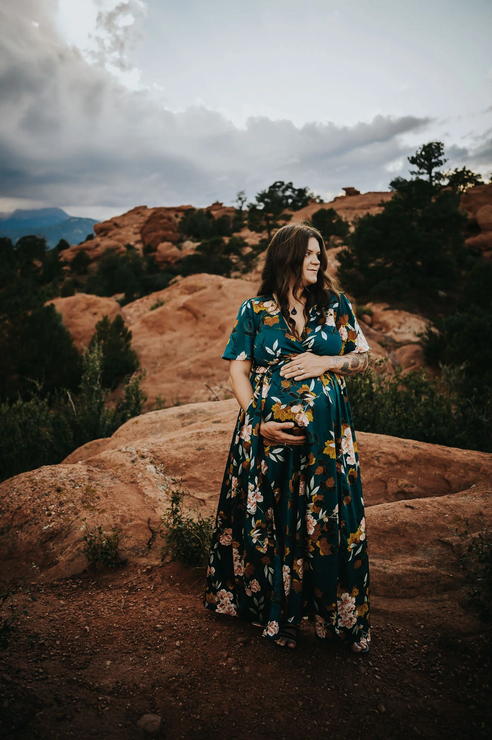 Pregnant woman in a floral dress standing among the red rock formations at Garden of the Gods in Colorado Springs.