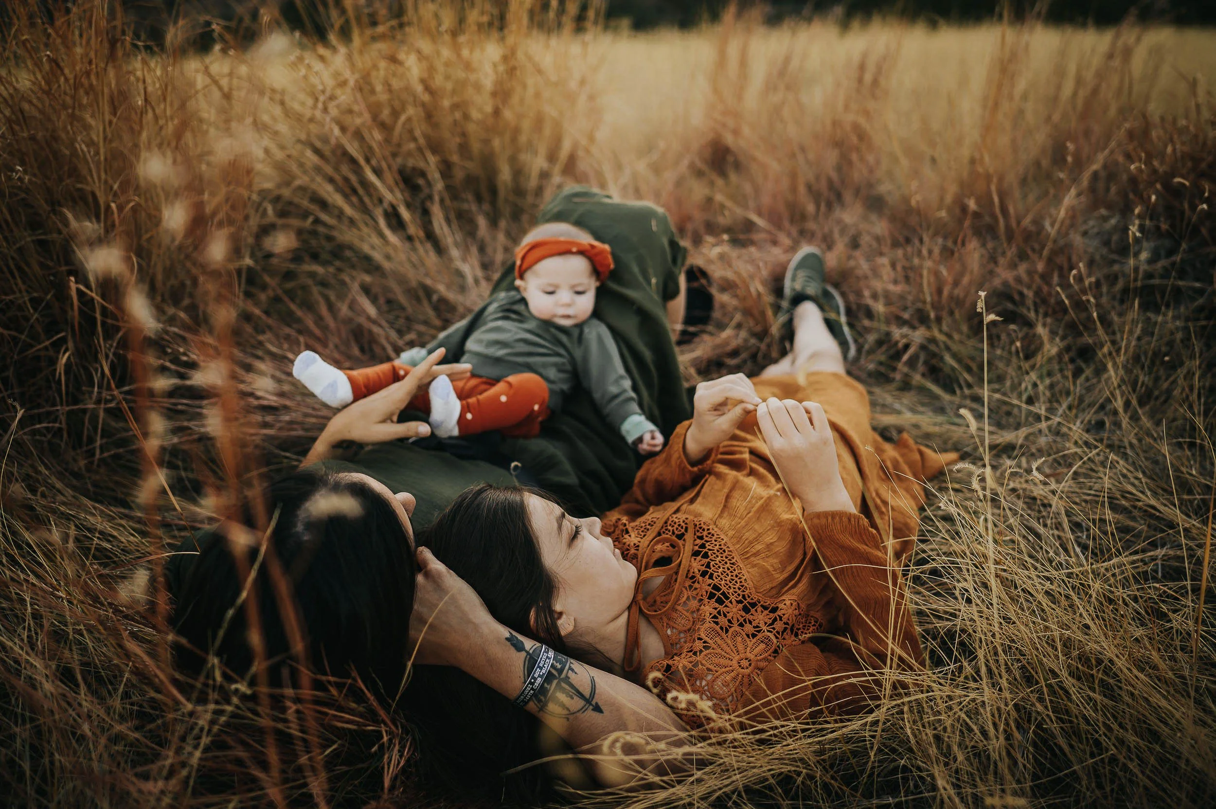 Mom and two children in a fall setting, coordinated in rust and cream with child in orange knit beanie, reading together among autumn foliage.