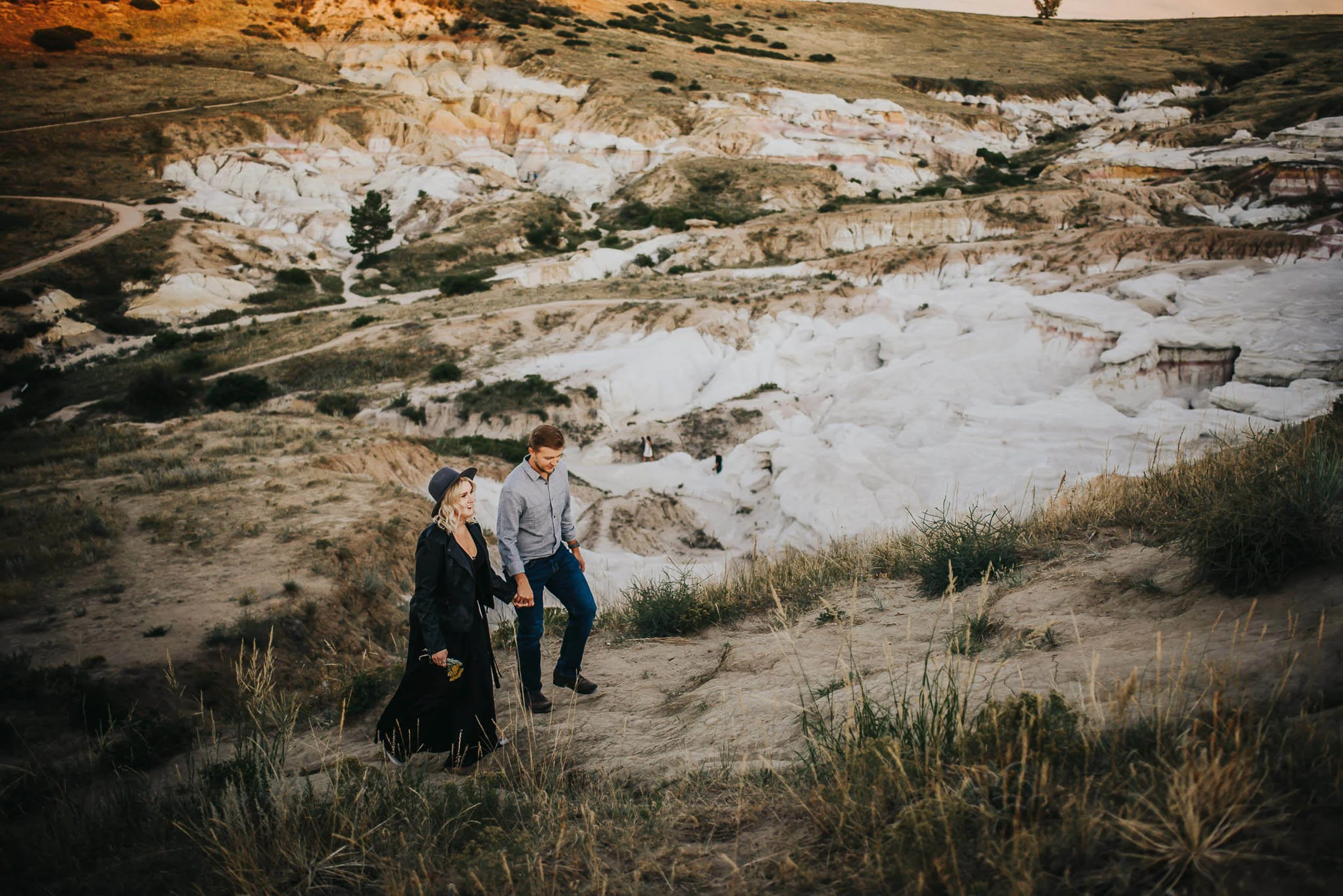 A couple stands together in a striking white and ochre painted hills landscape at The Paint Mines Park.