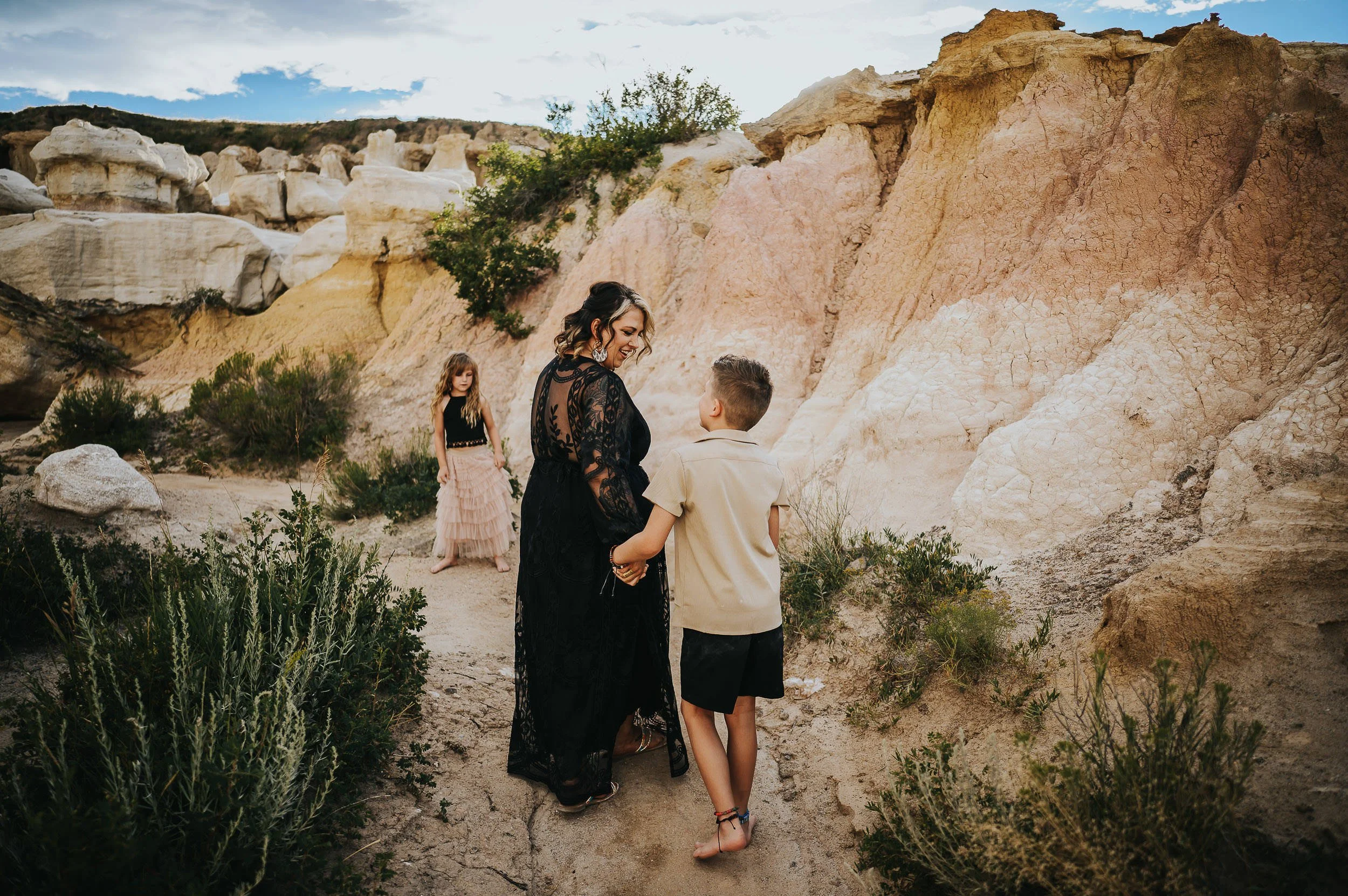 Family exploring Paint Mines rock formations in Colorado, mom in black lace dress holding hands with son while daughter walks ahead.