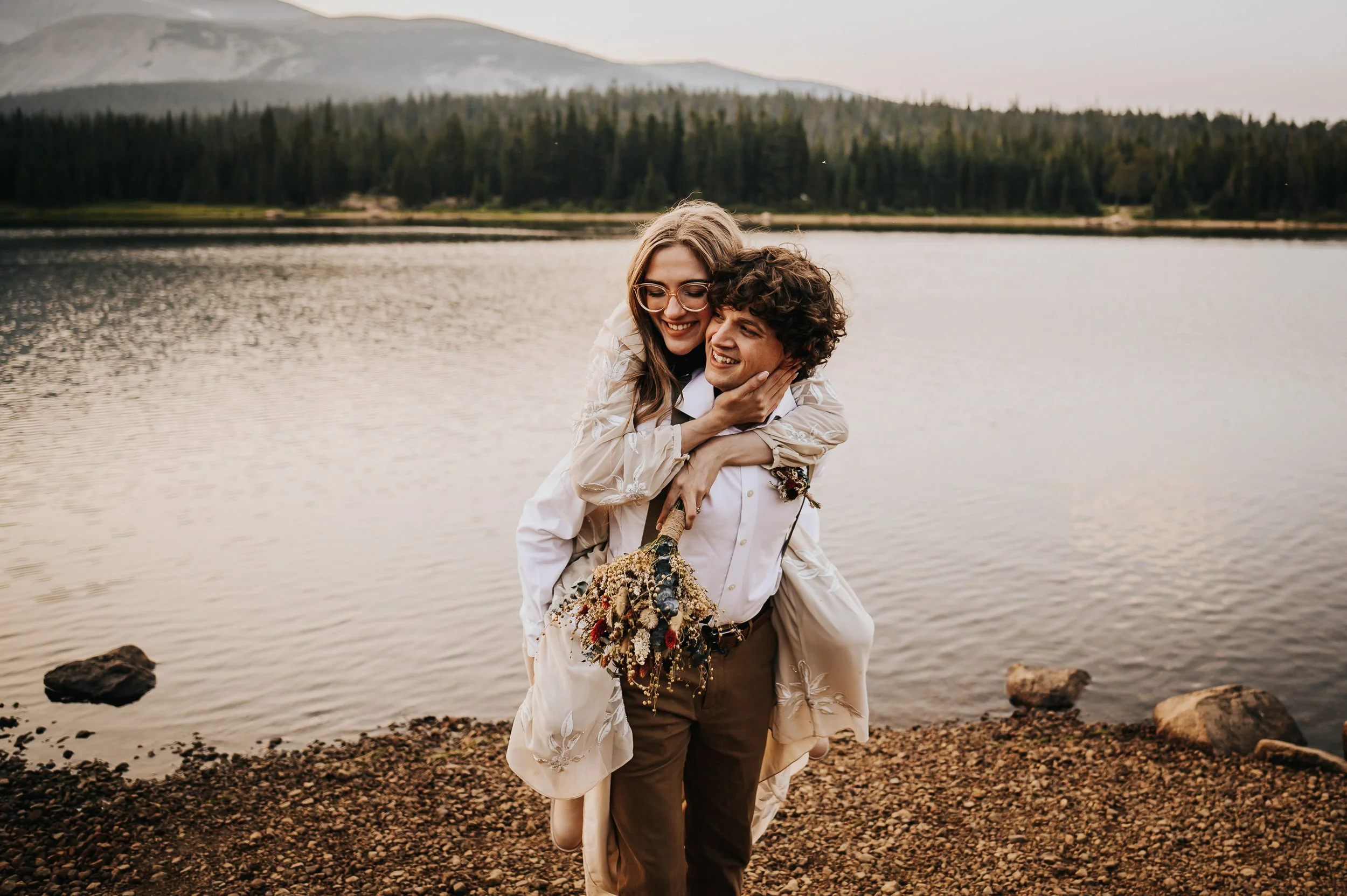 A couple embraces and laughs together at the edge of a Colorado mountain lake, fall foliage behind them at Brainard Lake after their elopement.
