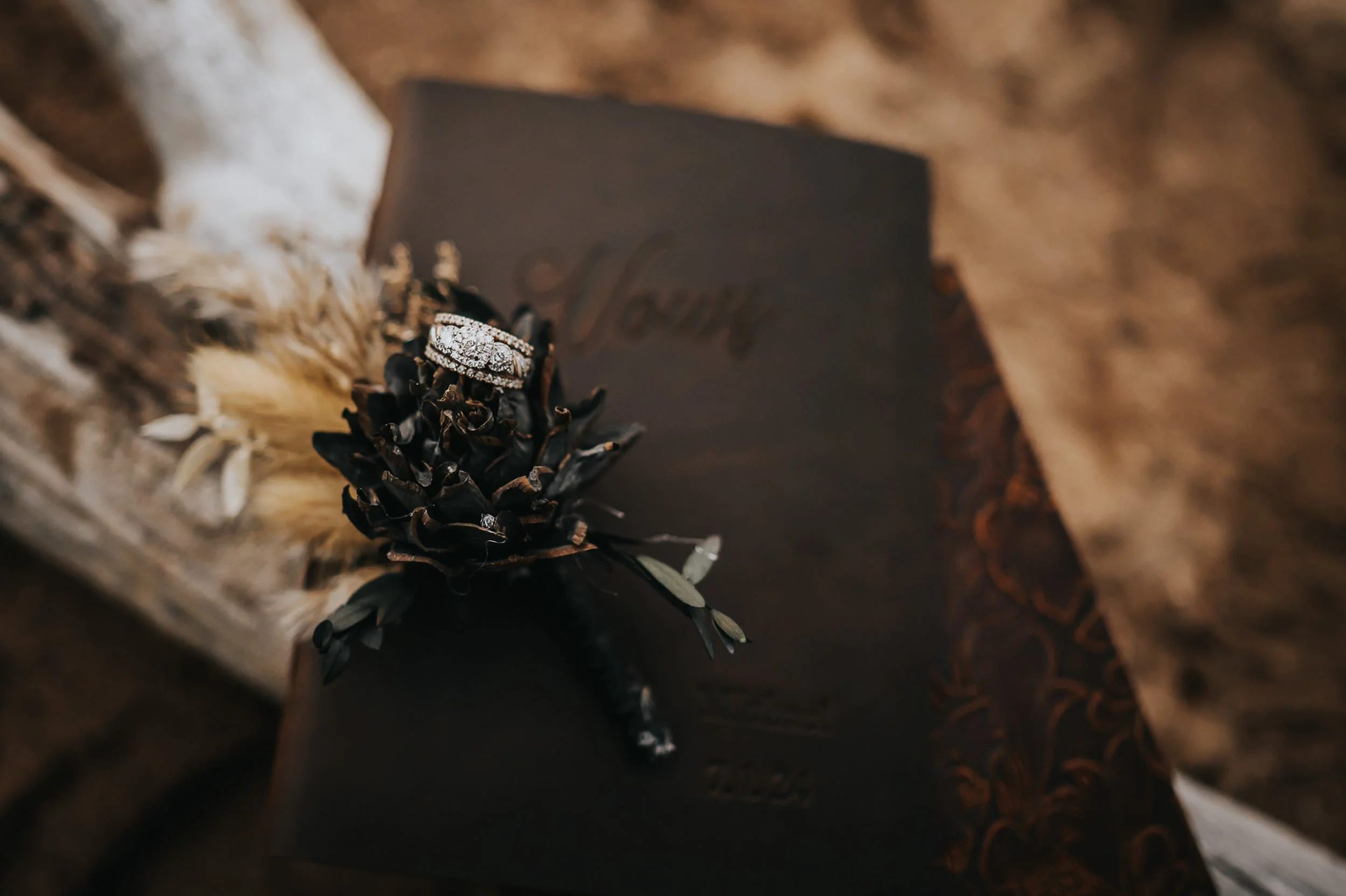 Close detail of a dark floral bouquet with a wedding ring and vow book resting on top.