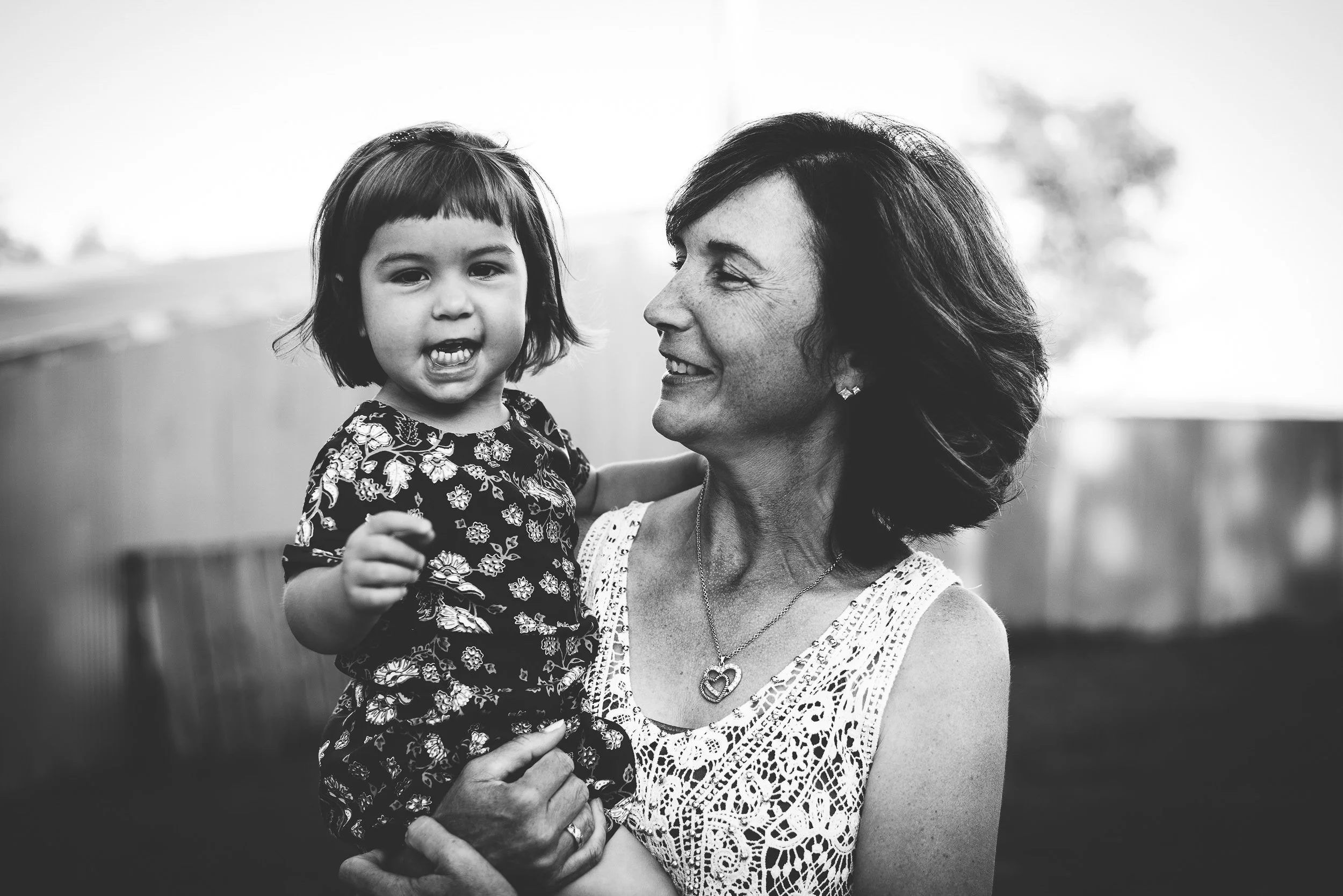 A mother and small daughter share a laugh outdoors, captured in black and white.