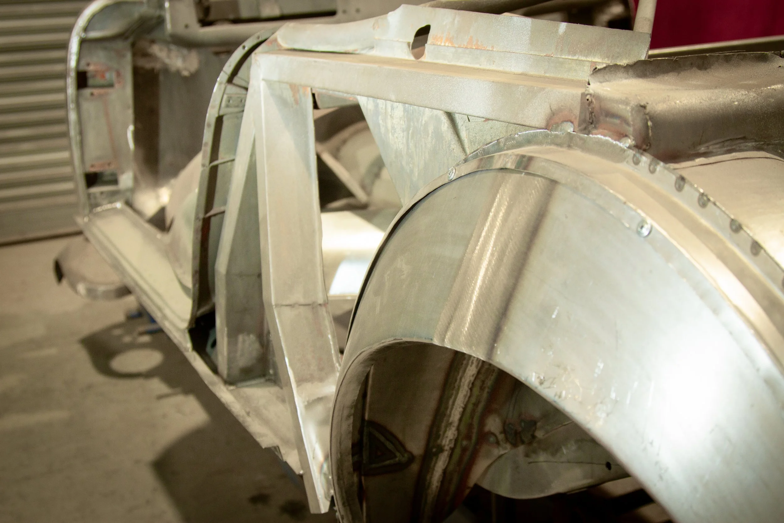 Close-up of a partially assembled metal car body with rivets and panels, in Alficina's metal workshop.