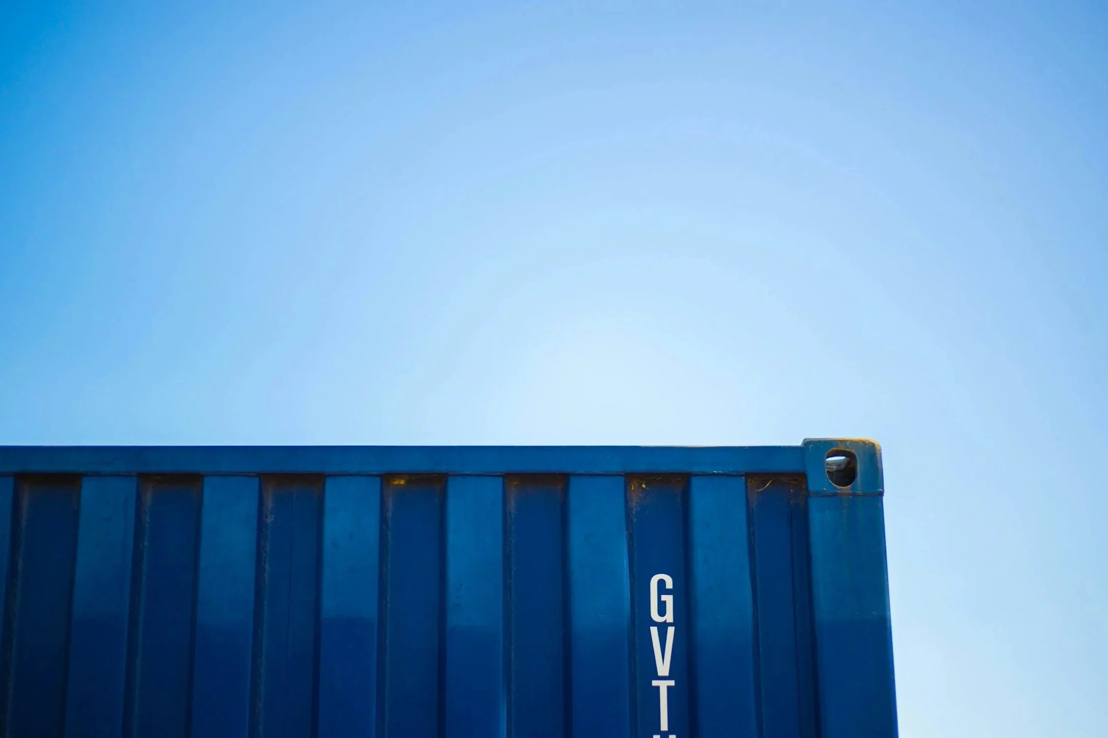 corner of a blue ship container with clear blue sky behind