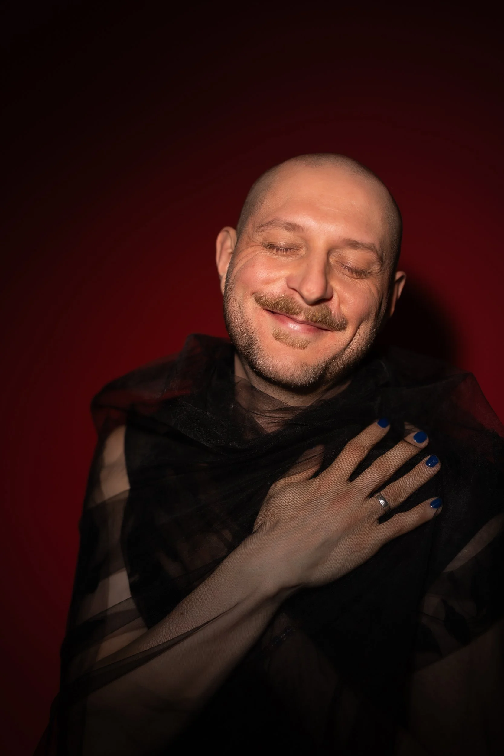 Portrait of Mikko. His eyes are closed and he is smiling. The light is soft and backdrop is in shadows.