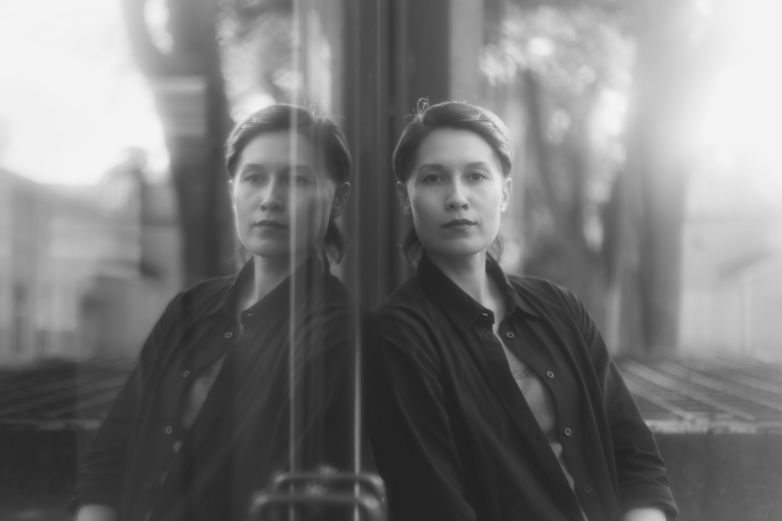 Black and white photo of a person looking at her reflection in a window.