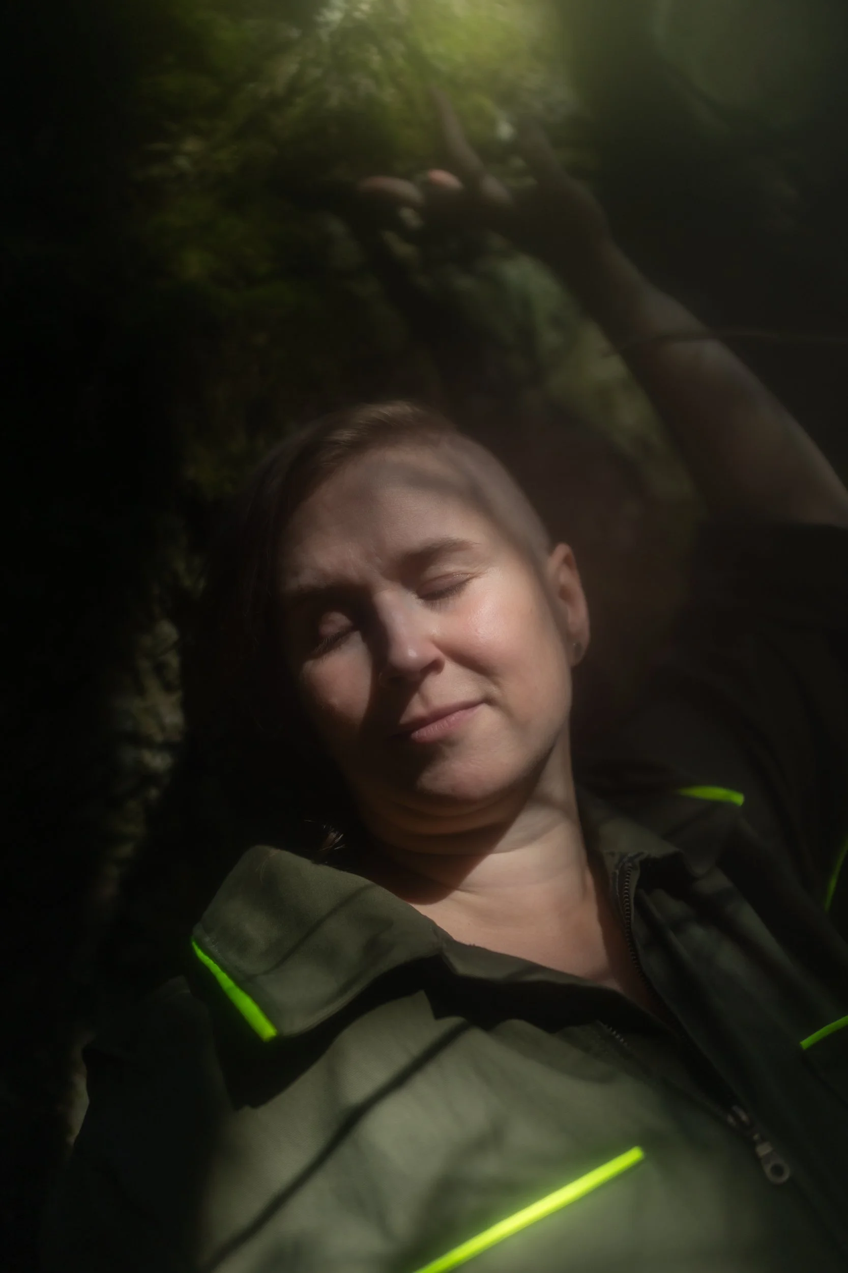 A person leans against a moss-covered rock. Their eyes are closed, and they have a dreamy expression. The image is soft and atmospheric.