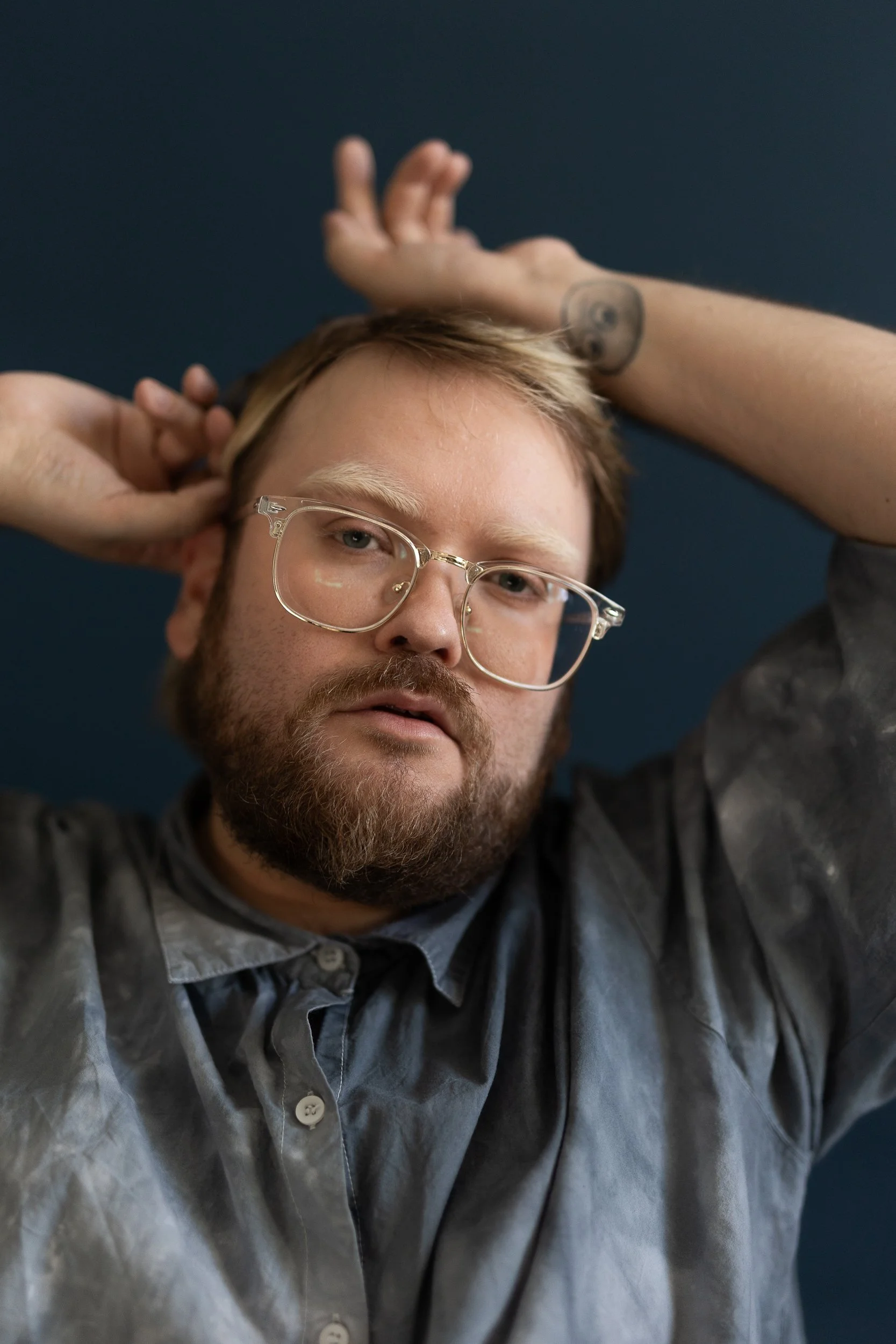 Portrait of Taneli Kemppi. Taneli is looking straight at the camera. The vibe is soft and tranquil. They are holding their hands at the top of their head palms facing up.