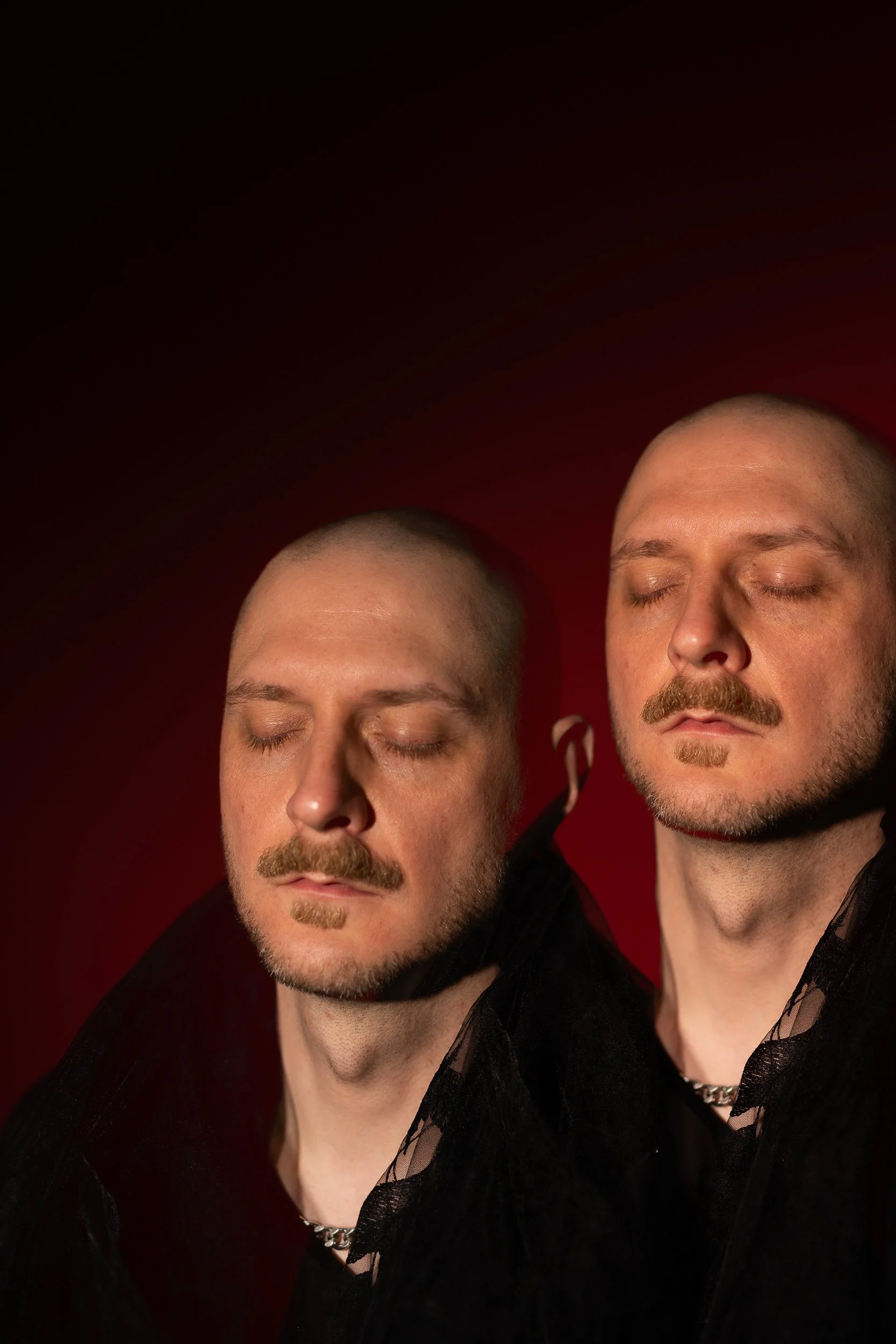 A double-exposure image in a studio. The person has their eyes closed and has a calm, sensitive, yet powerful expression. The image conveys sorrow and being on the threshold of something new.
