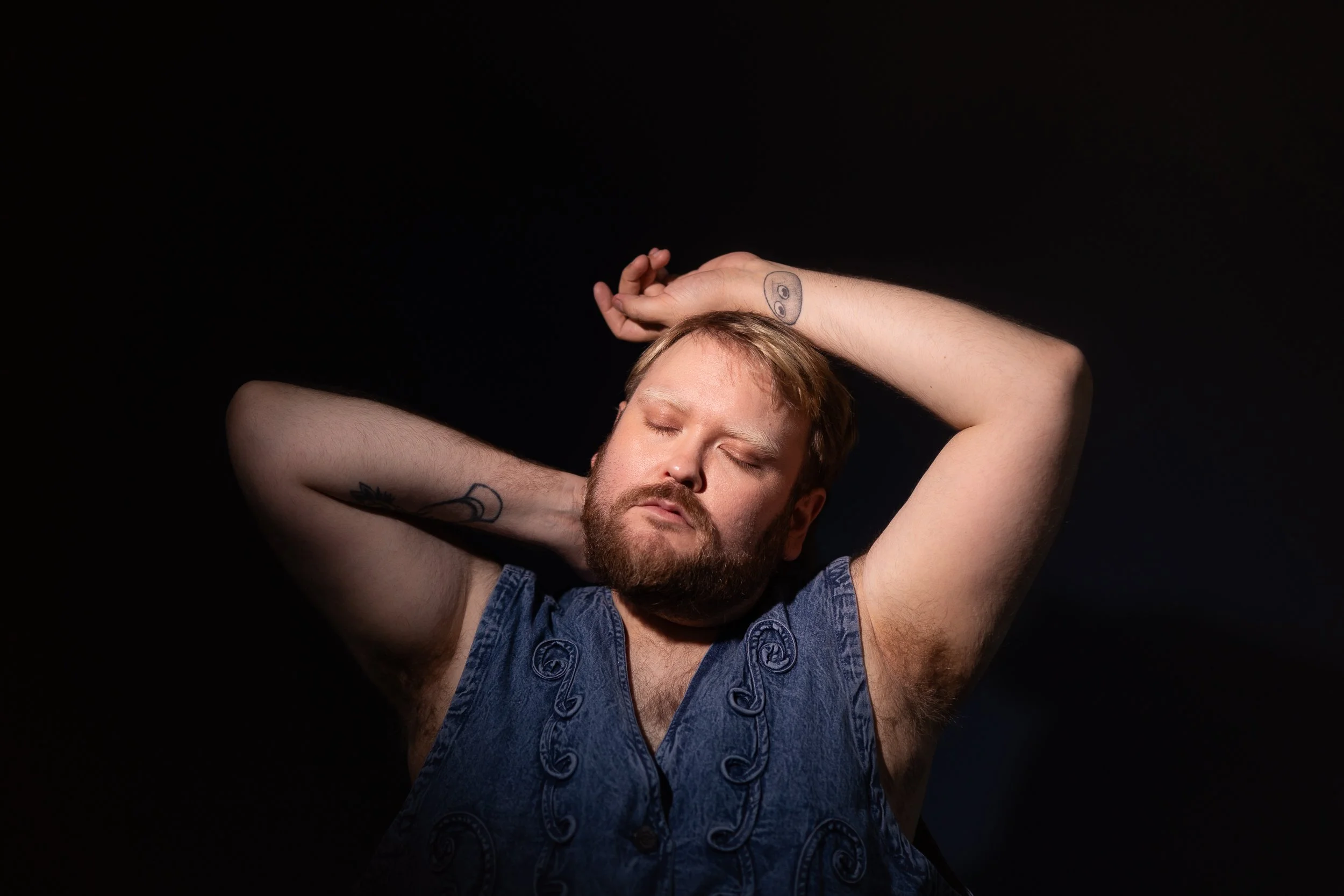 Softly lit portrait of a person standing against a black background with eyes closed and a calm, serene expression
