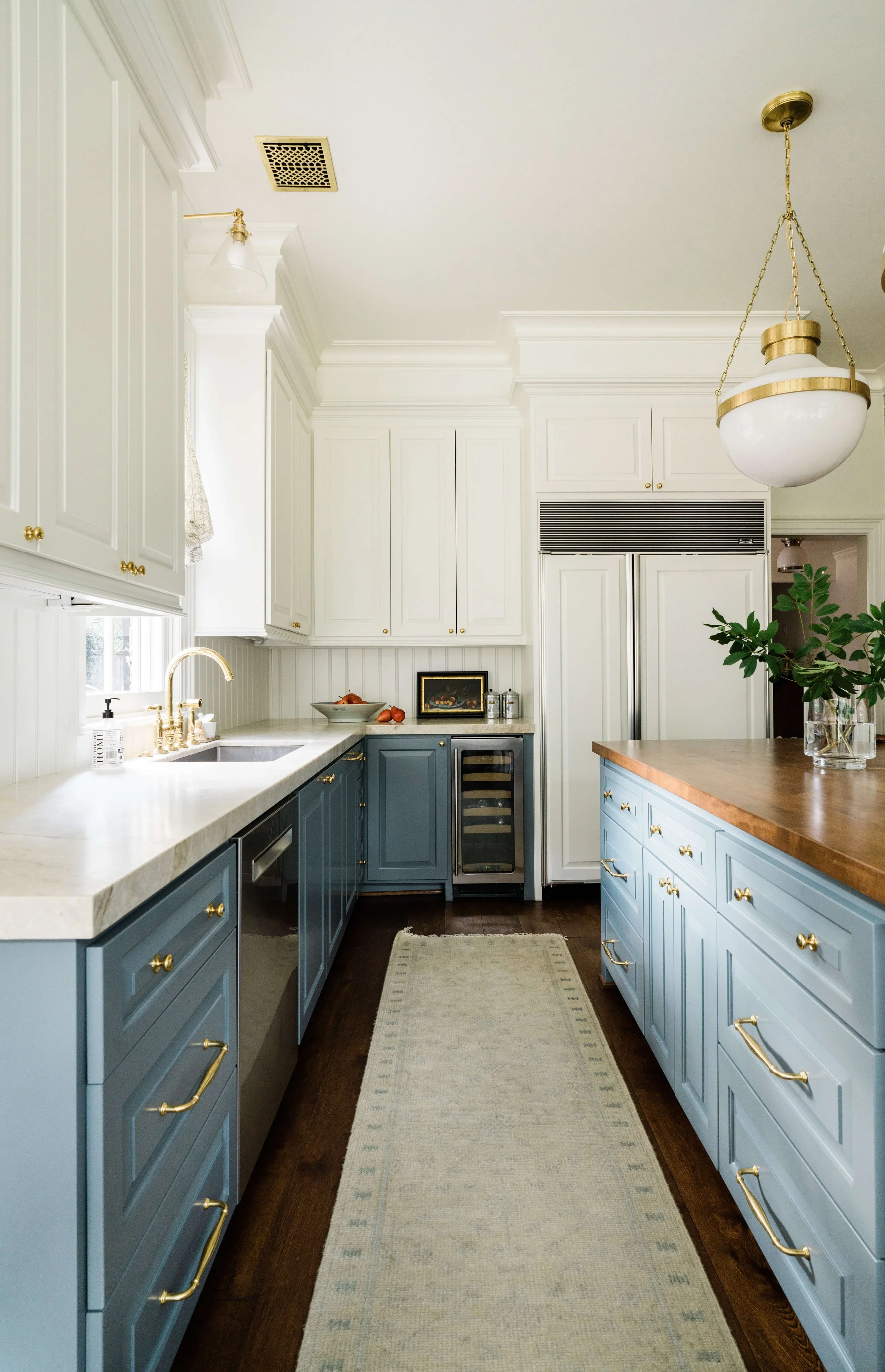A traditional kitchen with blue cabinetry and gold lighting with paneled refrigerator