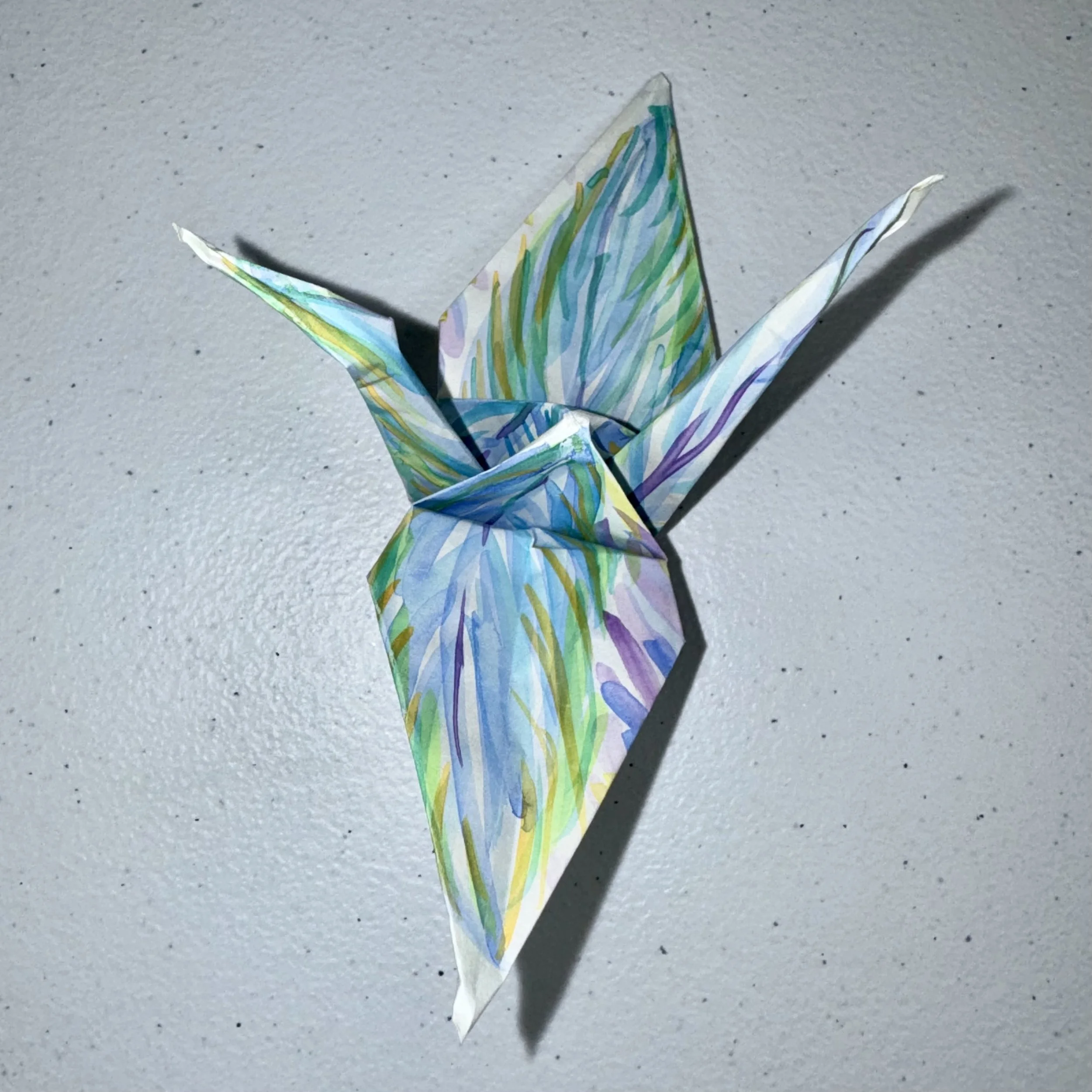 Colorful paper origami butterfly with shadow on a light gray textured surface.
