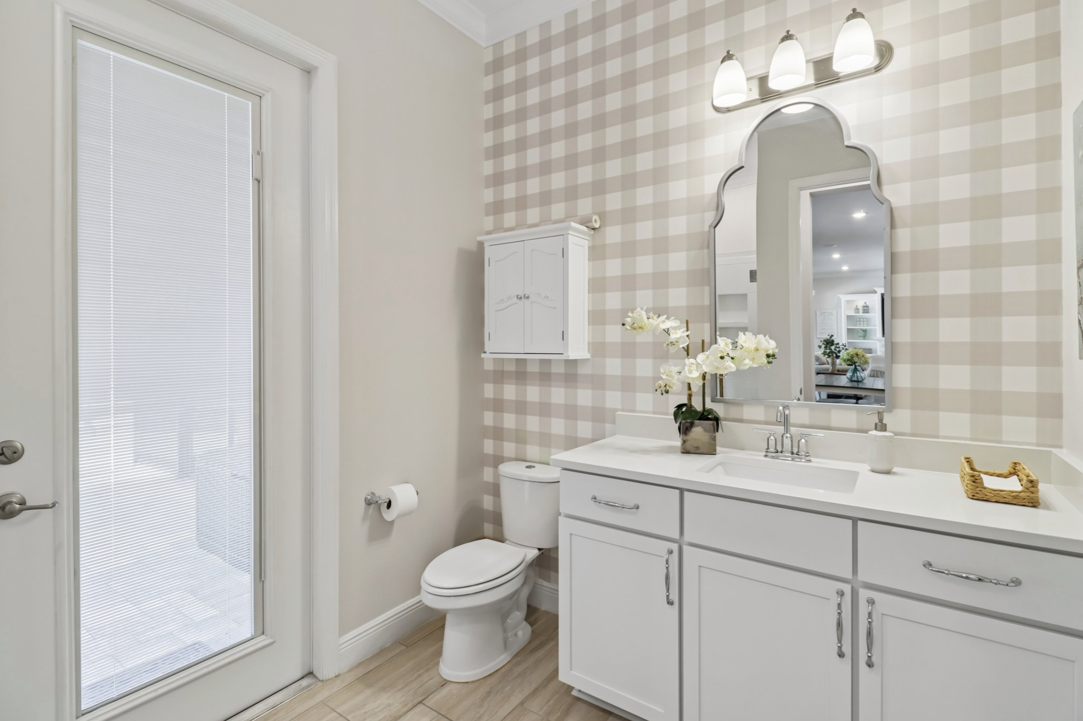 Bathroom with a sliding glass shower door, a white toilet, white vanity with a marble top, mirror, floral decoration, and patterned wallpaper.
