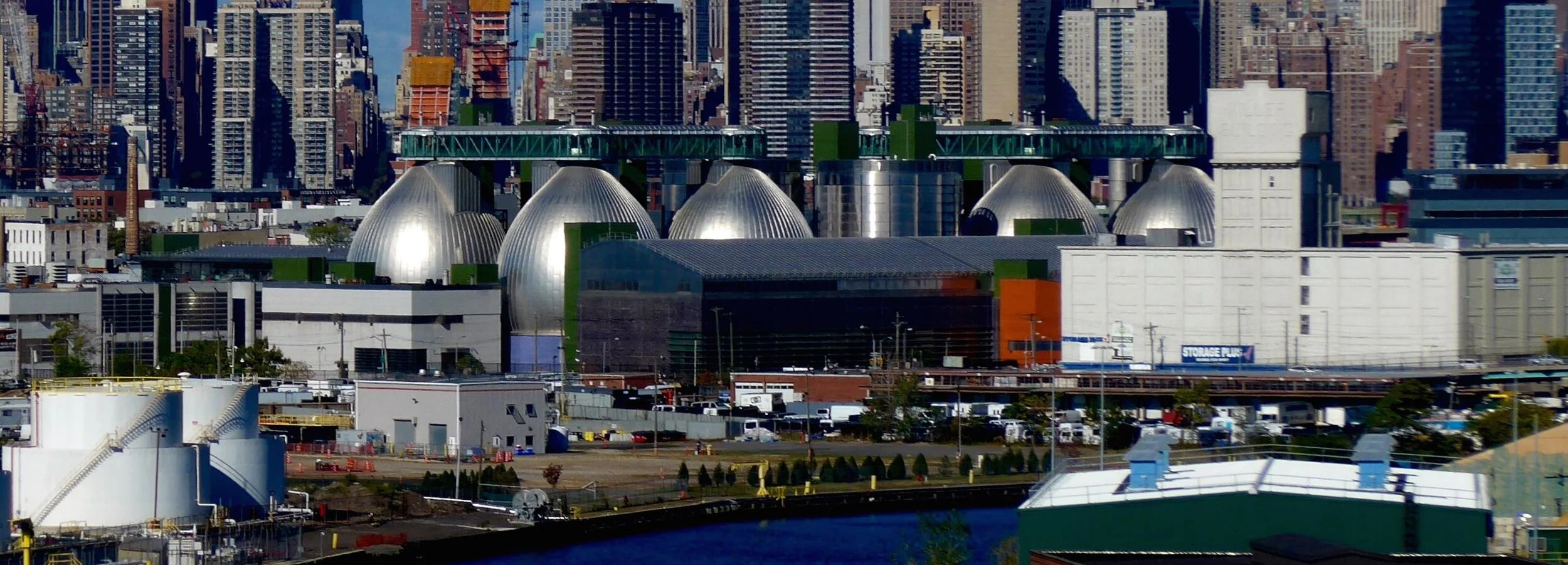 Side view of DEP’s Newtown Creek wastewater resource recovery facility with Newtown Creek in the foreground and metal water treatment towers in background. Source: DEP