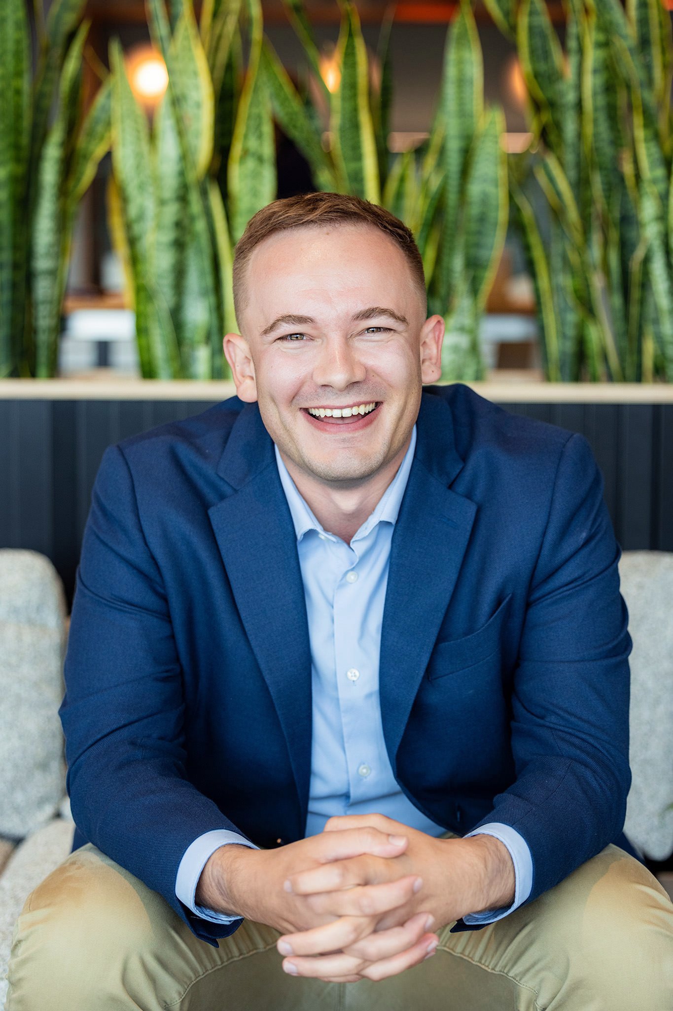Man in blue blazer posing for a headshot in front of greenery. 