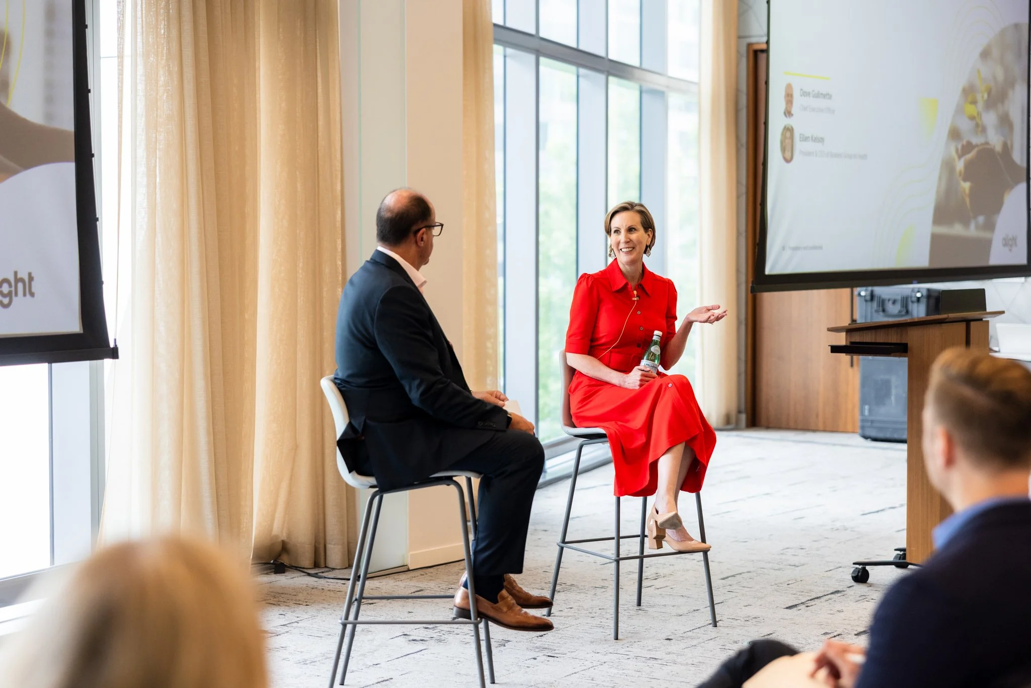 Woman in a red dress speaking to other male presenter during corporate seminar