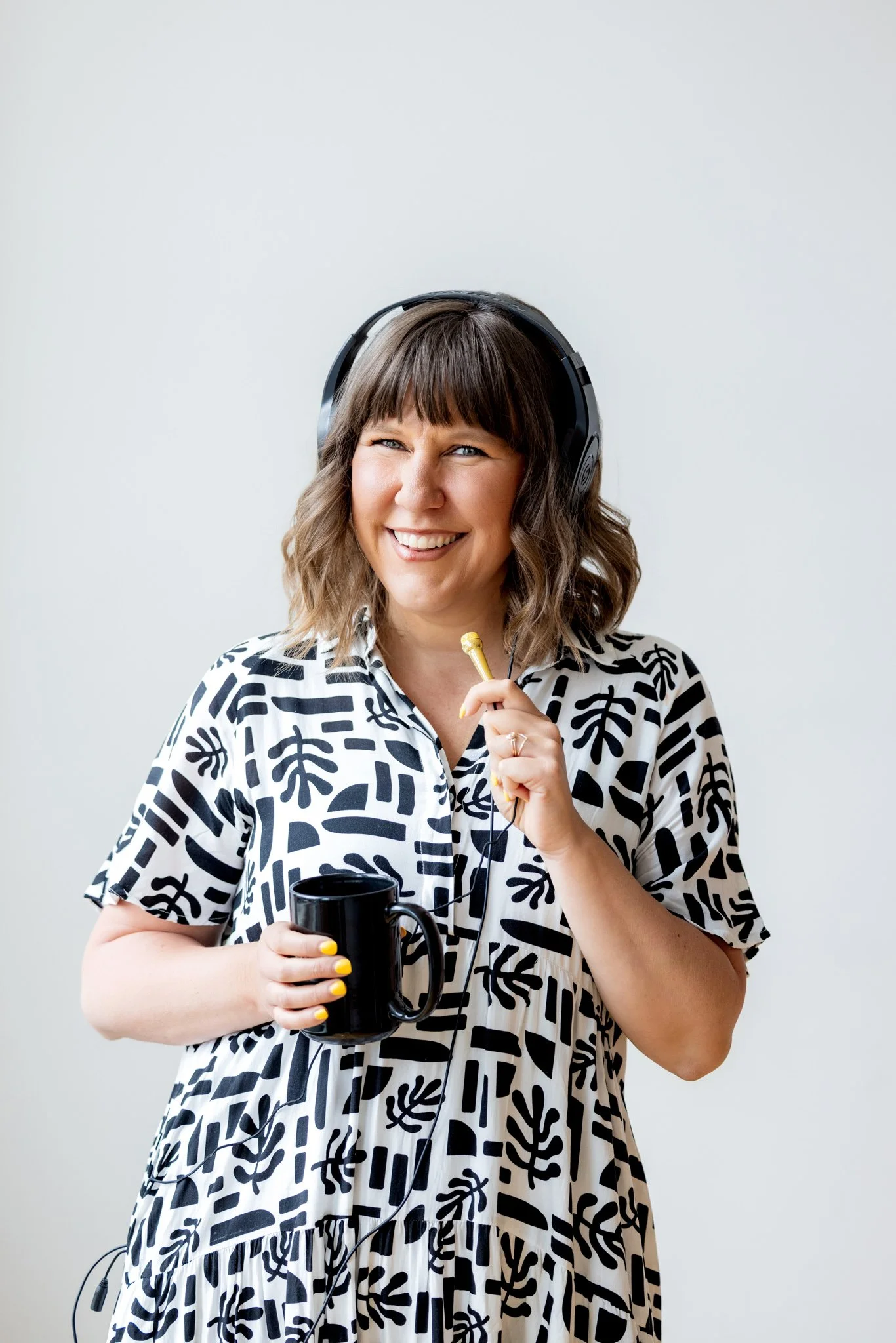Portrait of a woman in a black and white dress and headphones, holding a coffee cup