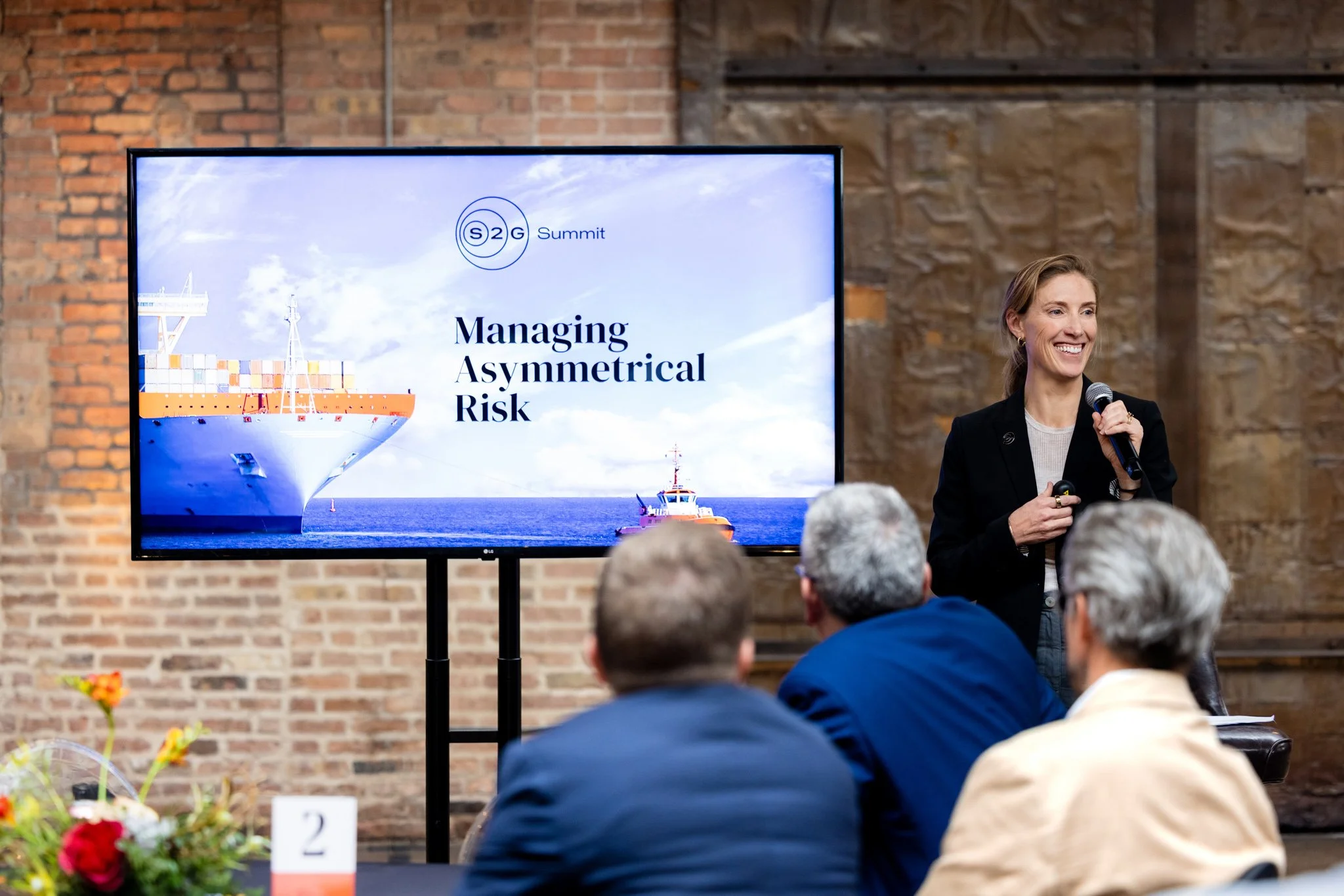 Smiling female presenter speaking to a group at a corporate seminar about managing asymmetrical risk