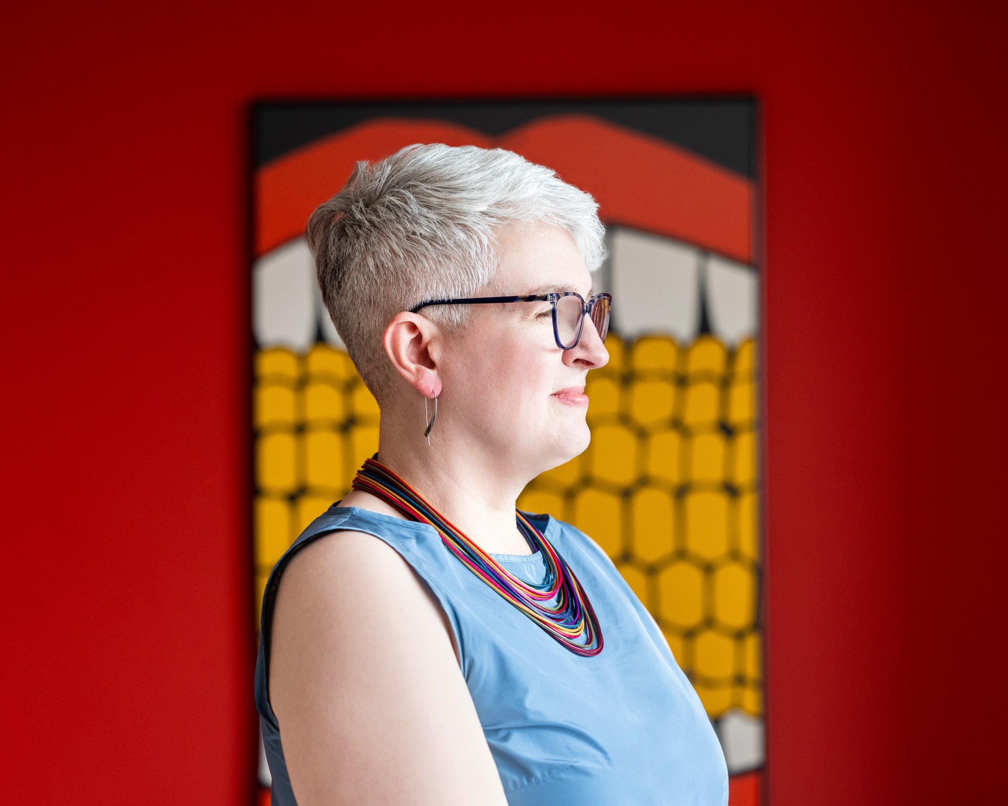Bold headshot of a female with short hair; taken in front of a red background with the subject in profile