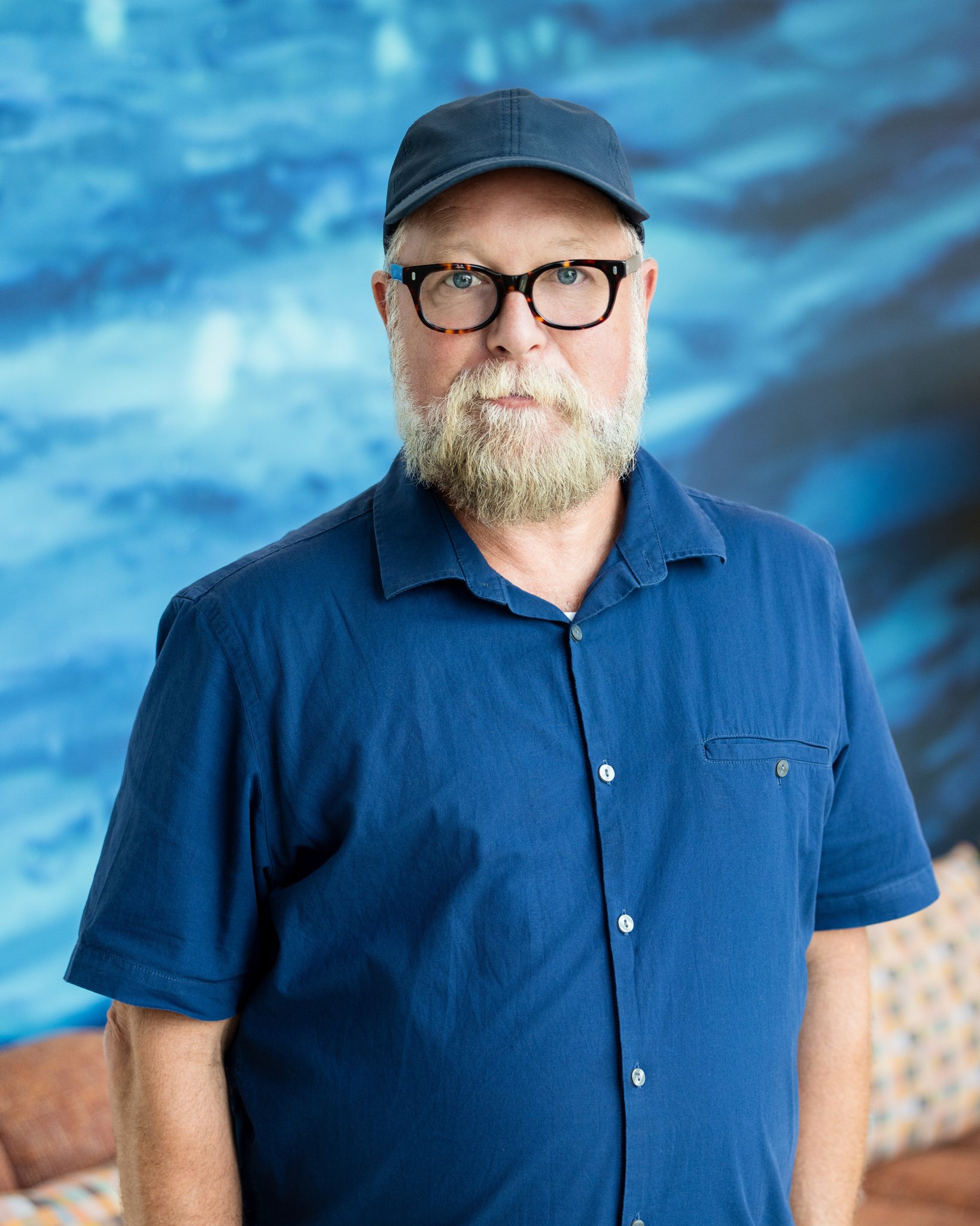 Environmental portrait of man with beard and ballcap against a blue painting