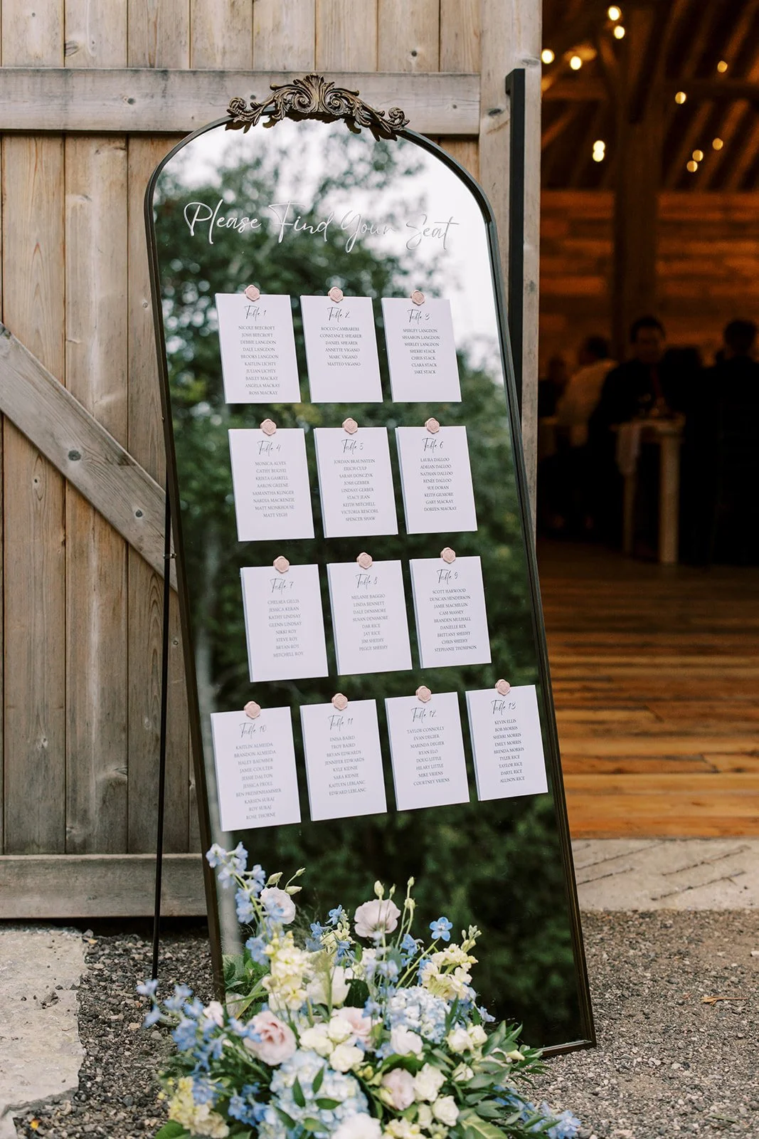 Barn wedding seating chart displayed on a mirror with floral arrangement and inTUNE Cambridge wedding DJs