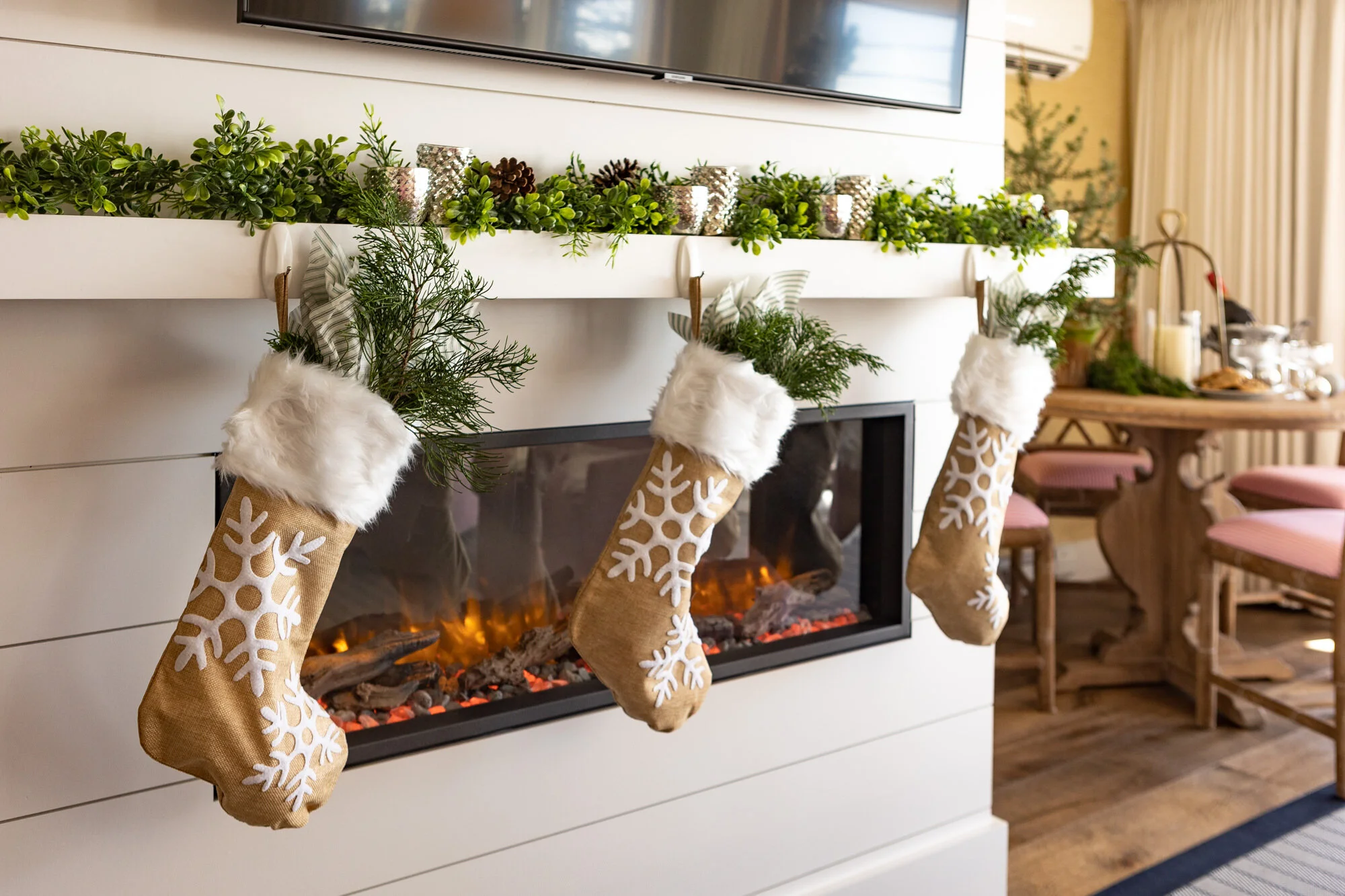 Christmas stockings hanging over a fireplace decorated with greenery and candles.