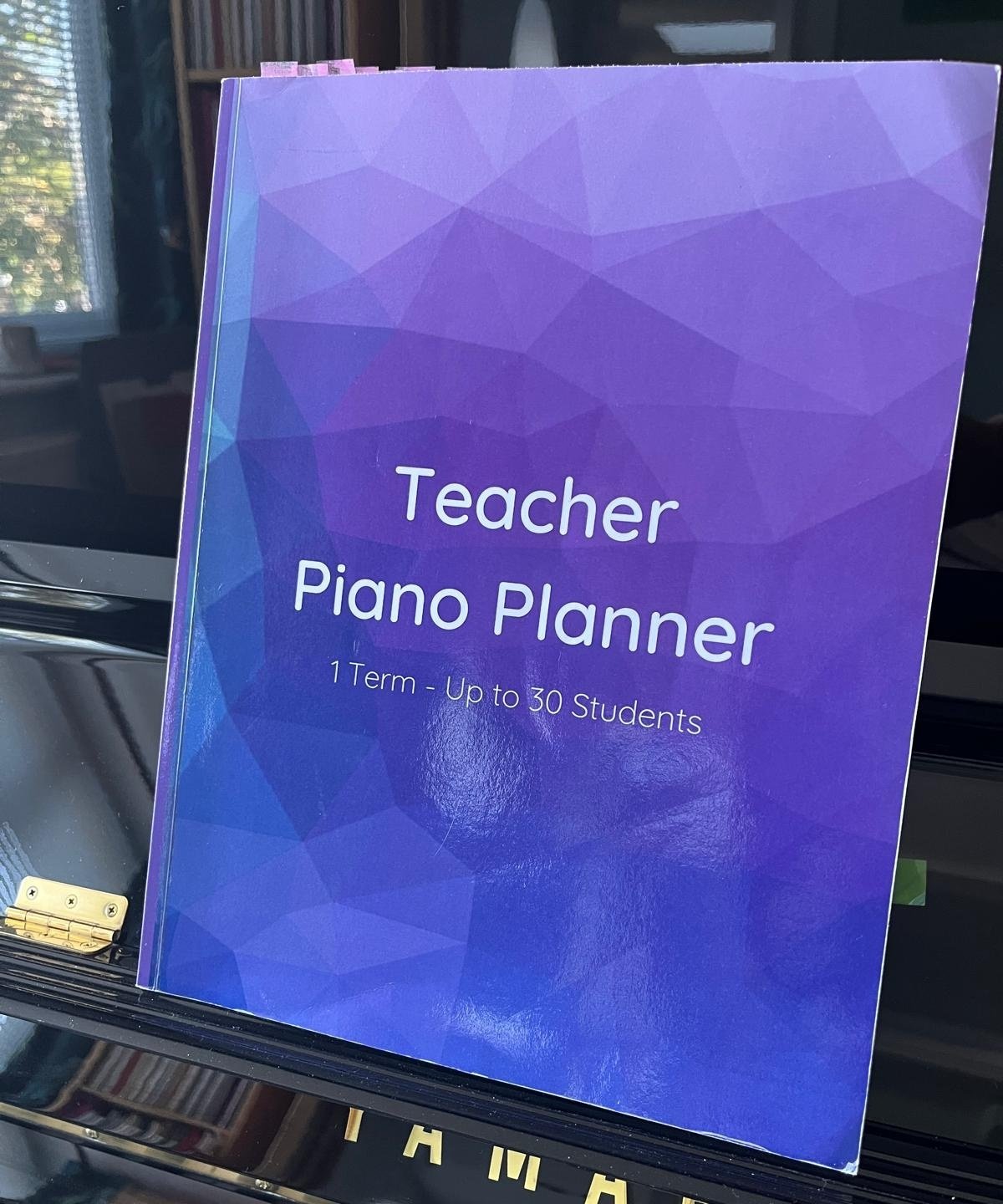 Purple Teacher Piano Planner resting on the music stand of a black Yamaha upright piano