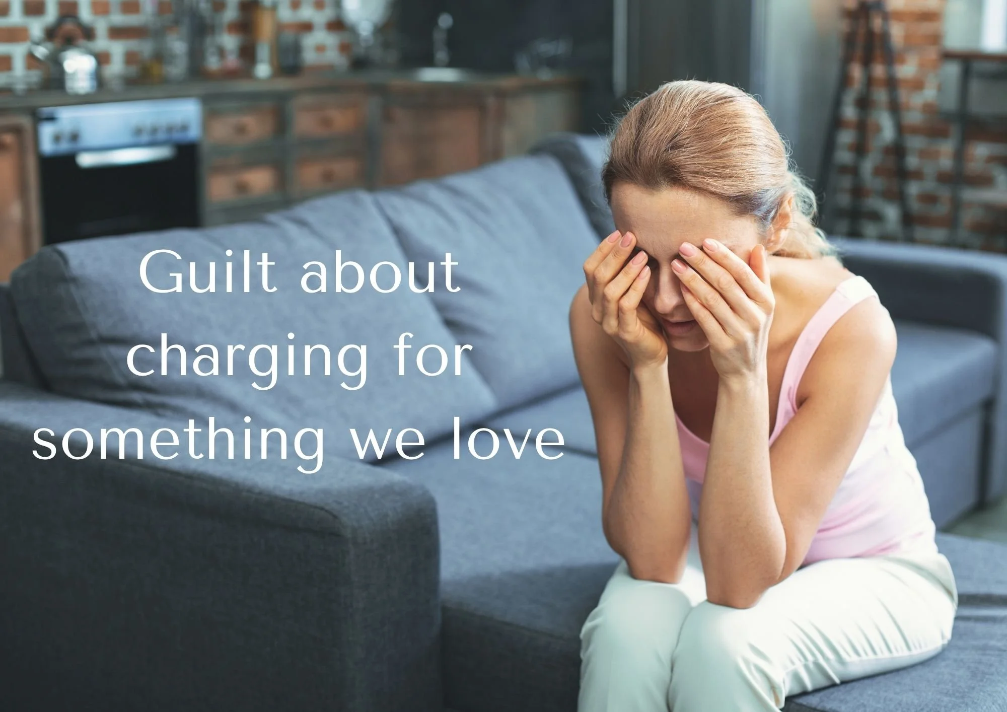 Woman sat on a grey sofa covering her eyes with her hands, resting her elbows on her knees, and text saying 'Guilt about charging for something we love'