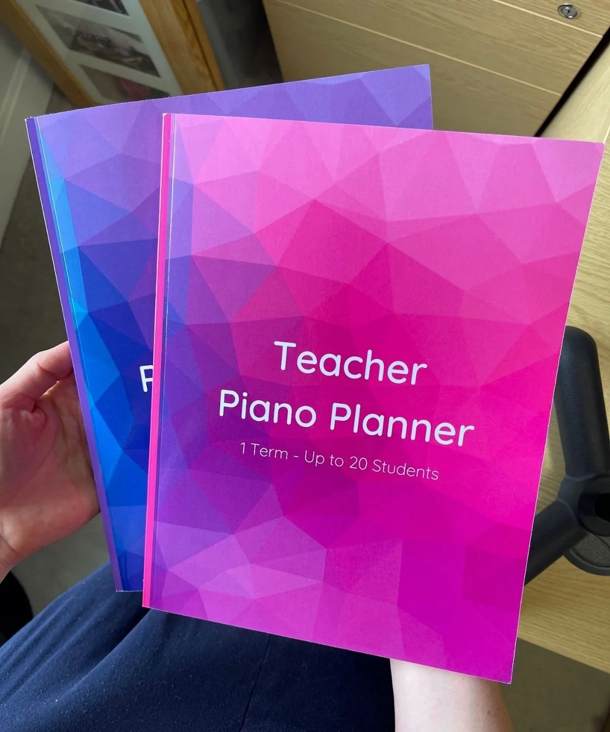 Two teacher piano planners being held up with the pink one in front and the purple one behind slightly offset diagonally