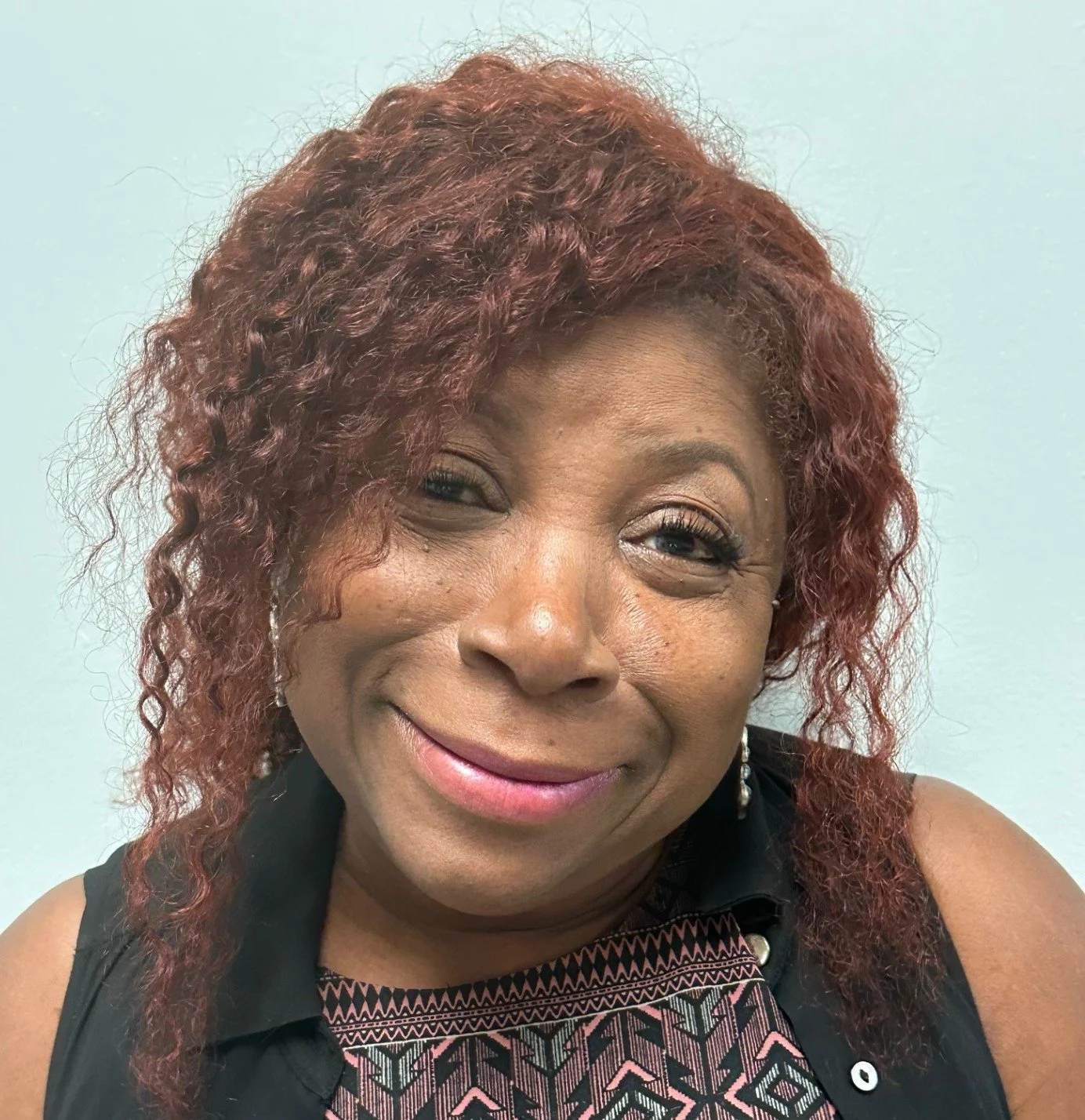 A woman with red curly hair wearing a pink collared shirt.