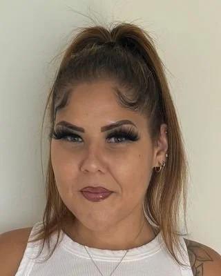 Portrait of a woman with long dark hair, wearing makeup and a striped shirt, smiling softly against a textured brown background.