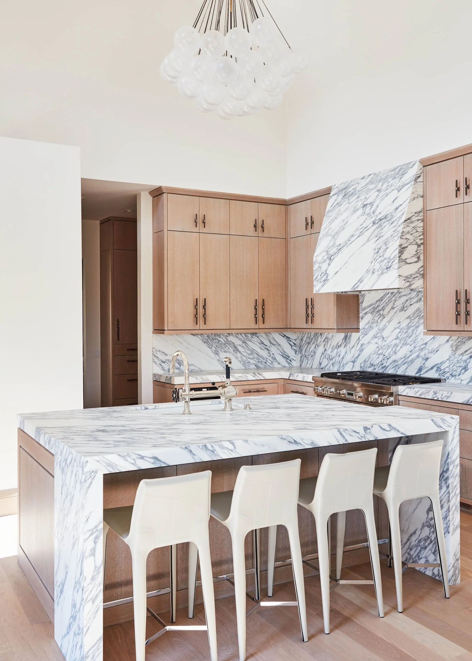  Marble countertops with matching island, backsplash and kitchen hood. Brown cabinets and white chairs.  