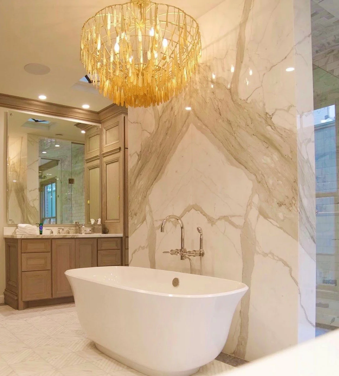  Bookmatched bathroom feature wall with white bathtub and gold chandelier.  